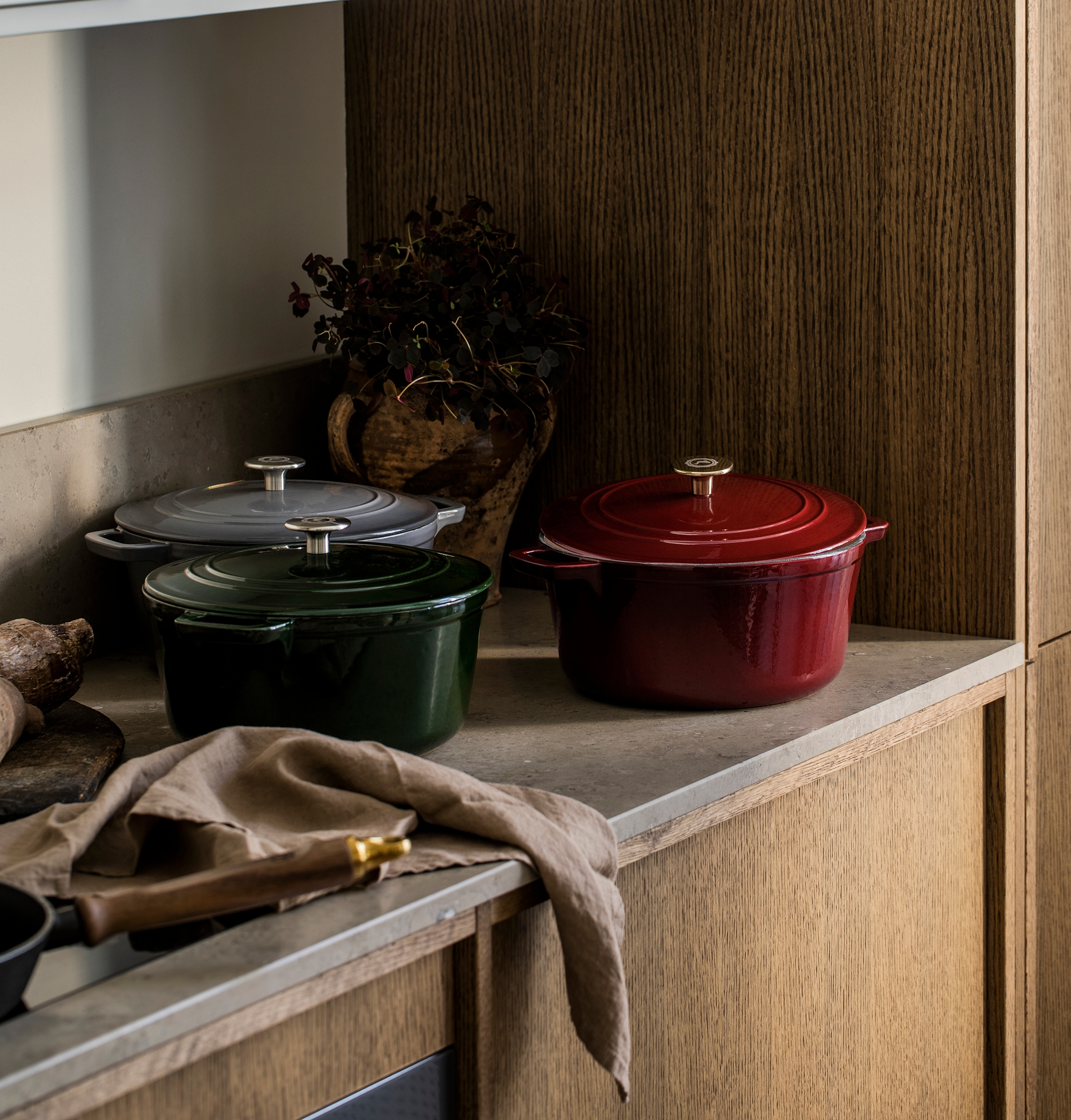 Tre röda, gröna och grå gjutjärnsgrytor på en köksbänkskiva.