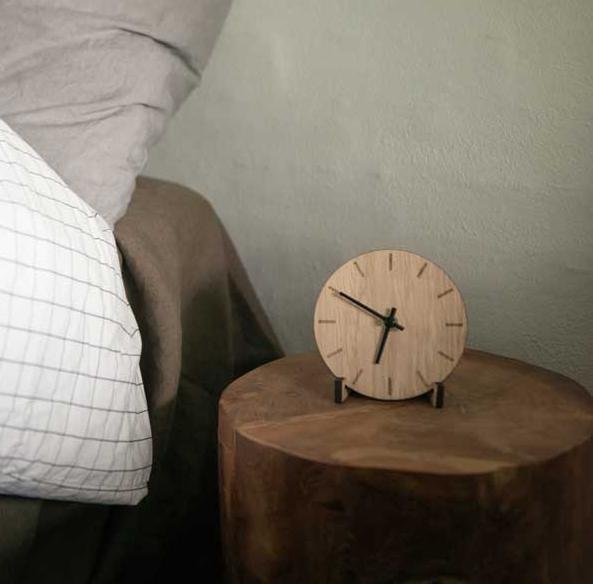 Rund träklocka på ett trädstubbebord bredvid en säng.