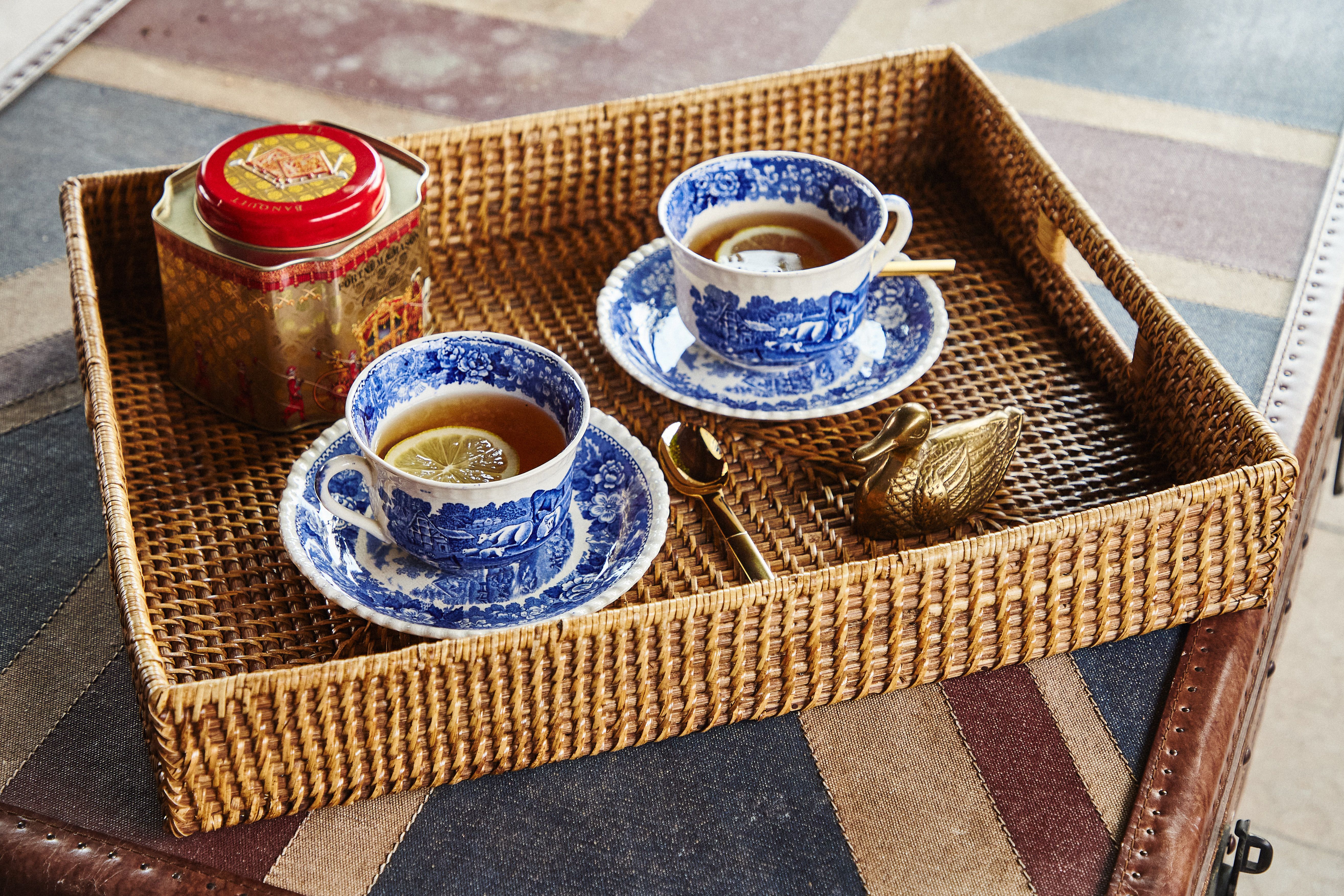 Två blåvita tekoppar med citron, en teburk och en gyllene svan på en flätad bricka över ett Union Jack-mönster