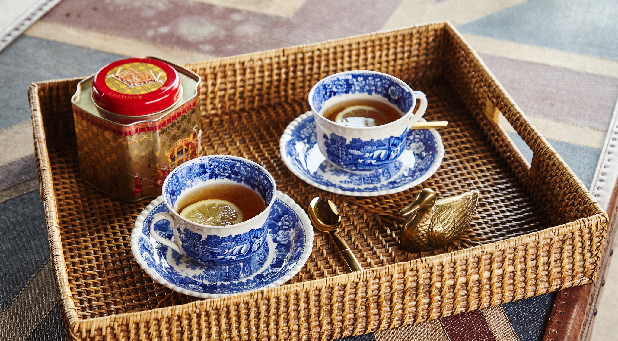 Två blåvita tekoppar med citron, en teburk och en gyllene svan på en flätad bricka över ett Union Jack-mönster