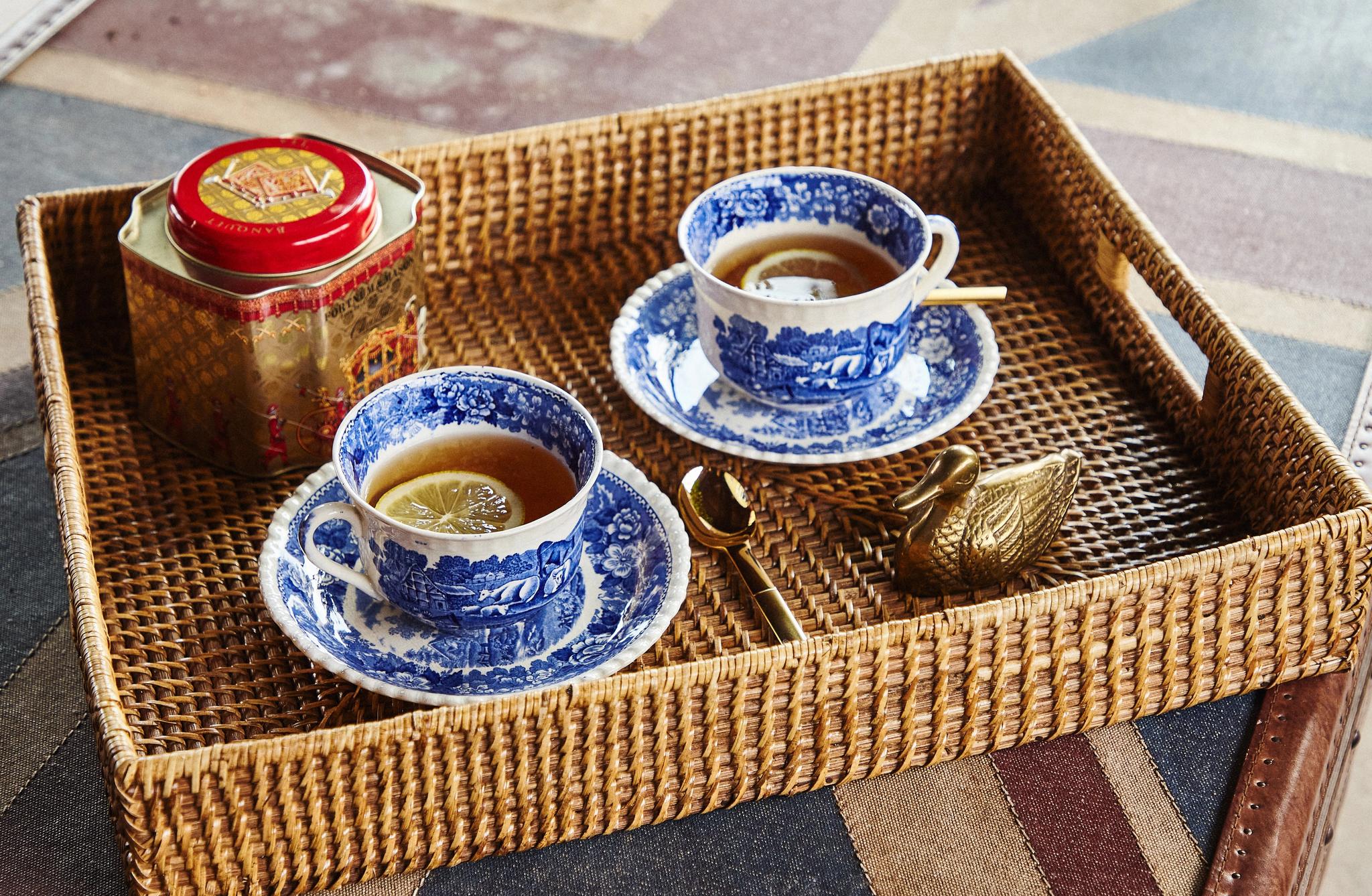 Två blåvita tekoppar med citron, en teburk och en gyllene svan på en flätad bricka över ett Union Jack-mönster