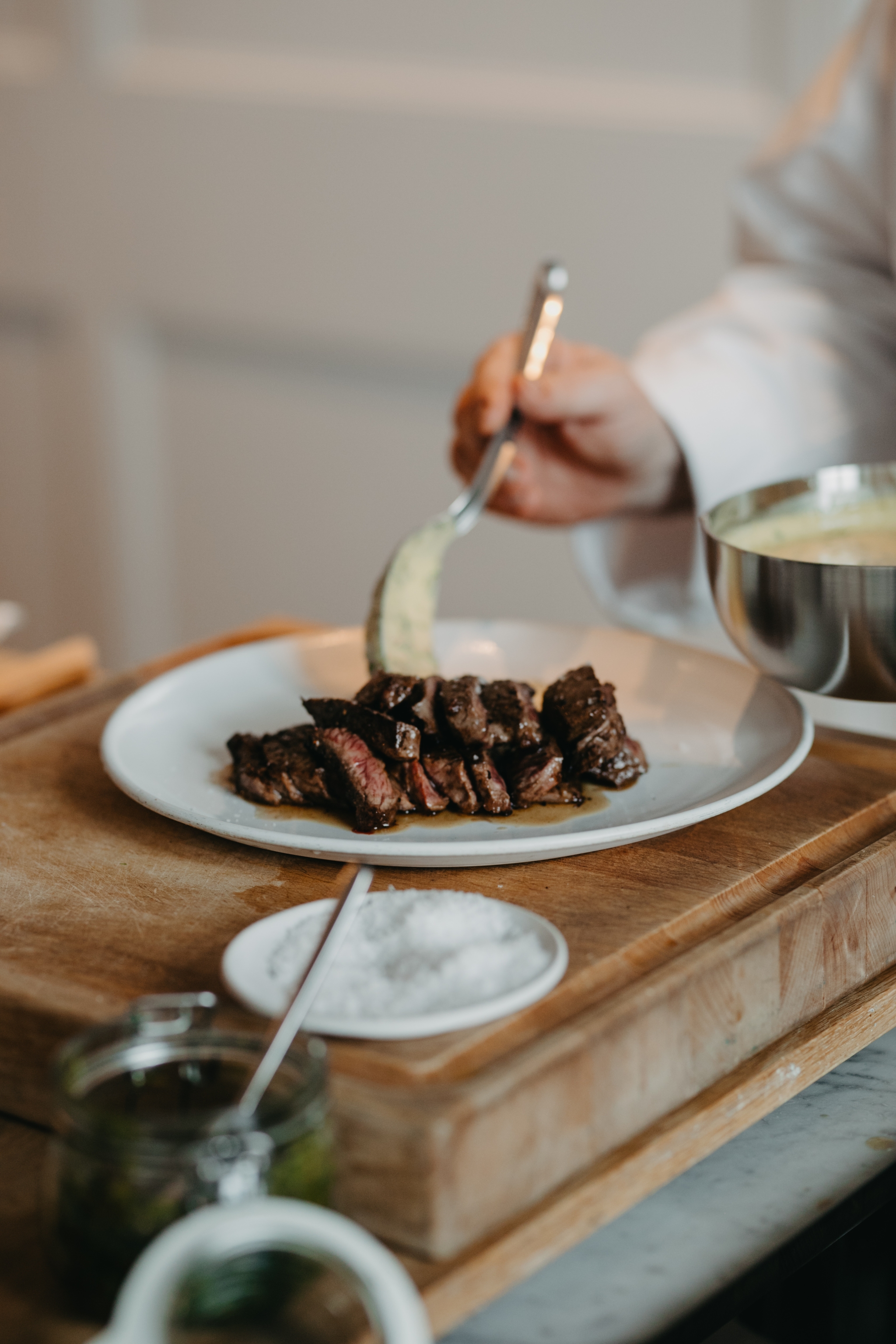 En kock skedar upp en krämig sidorätt med skivad biff på en tallrik.