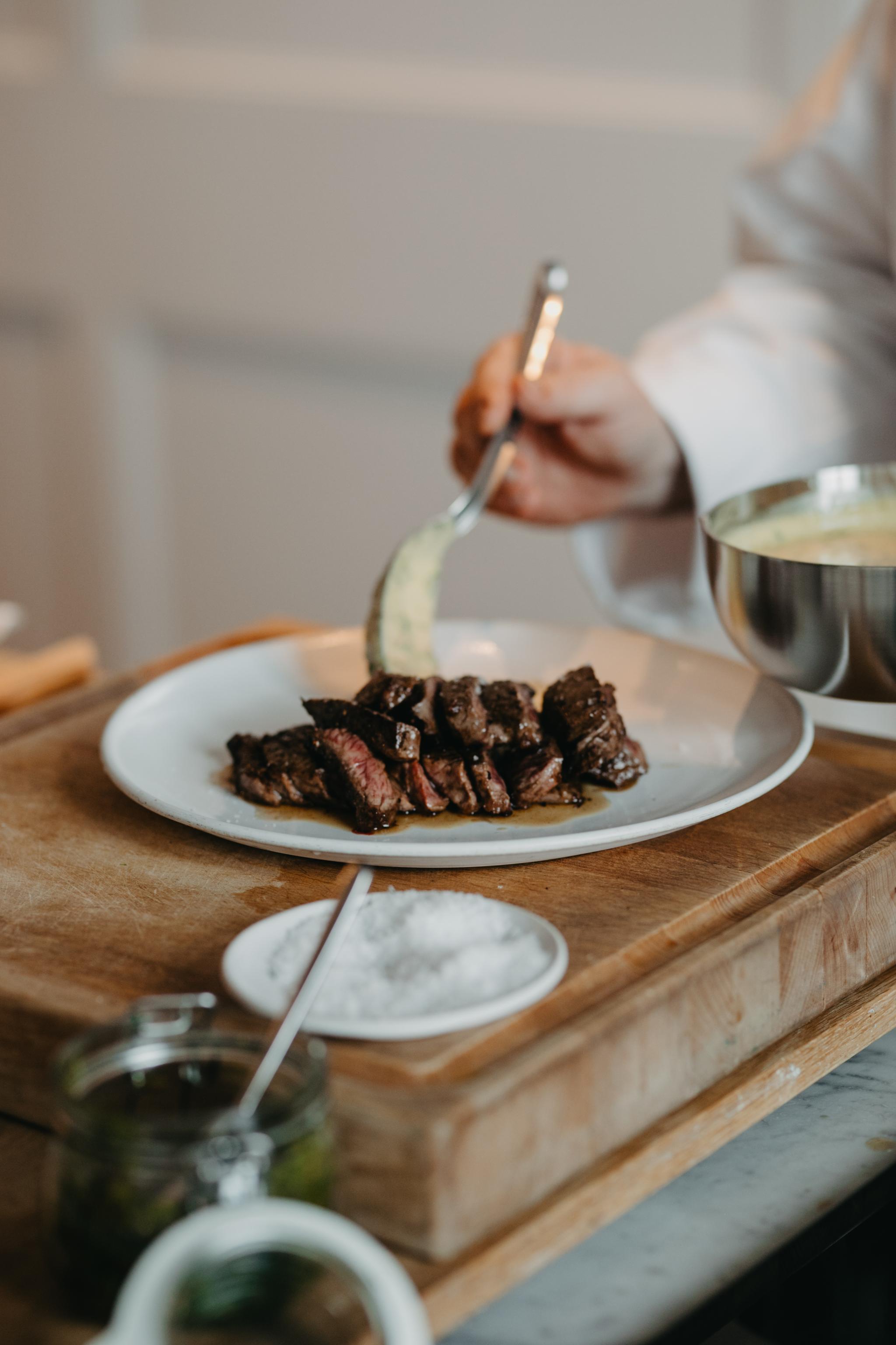 En kock skedar upp en krämig sidorätt med skivad biff på en tallrik.