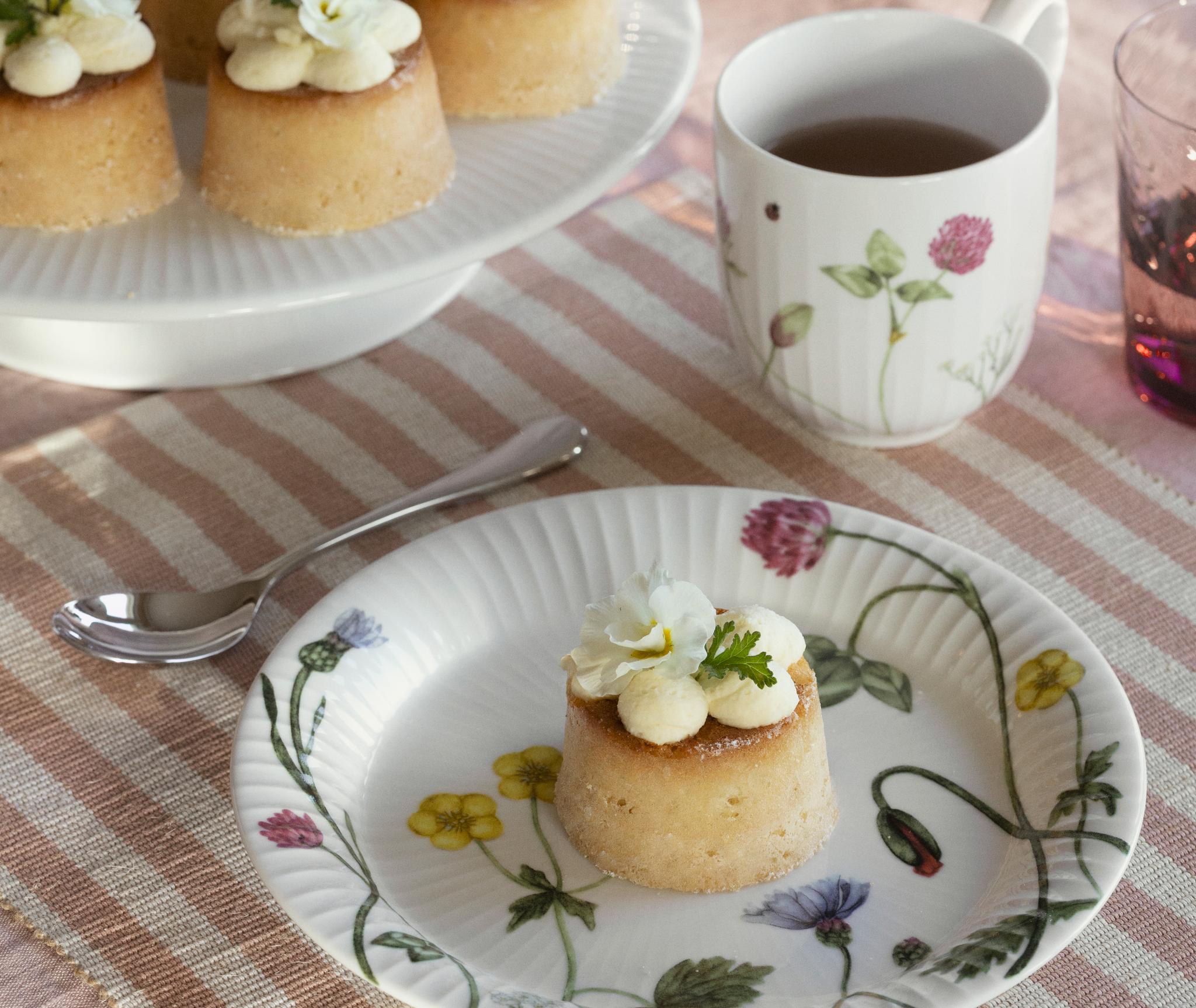Dukad fikabord med små bakelser dekorerade med blommor, te i blommiga koppar samt skålar med jordgubbar och citroner.