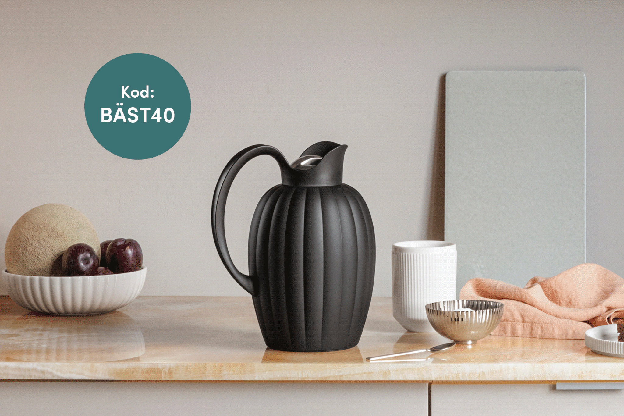 Black fluted thermal carafe on a countertop with a bowl of fruit and other ribbed kitchen items, with a "Kod: BÄST40" overlay.