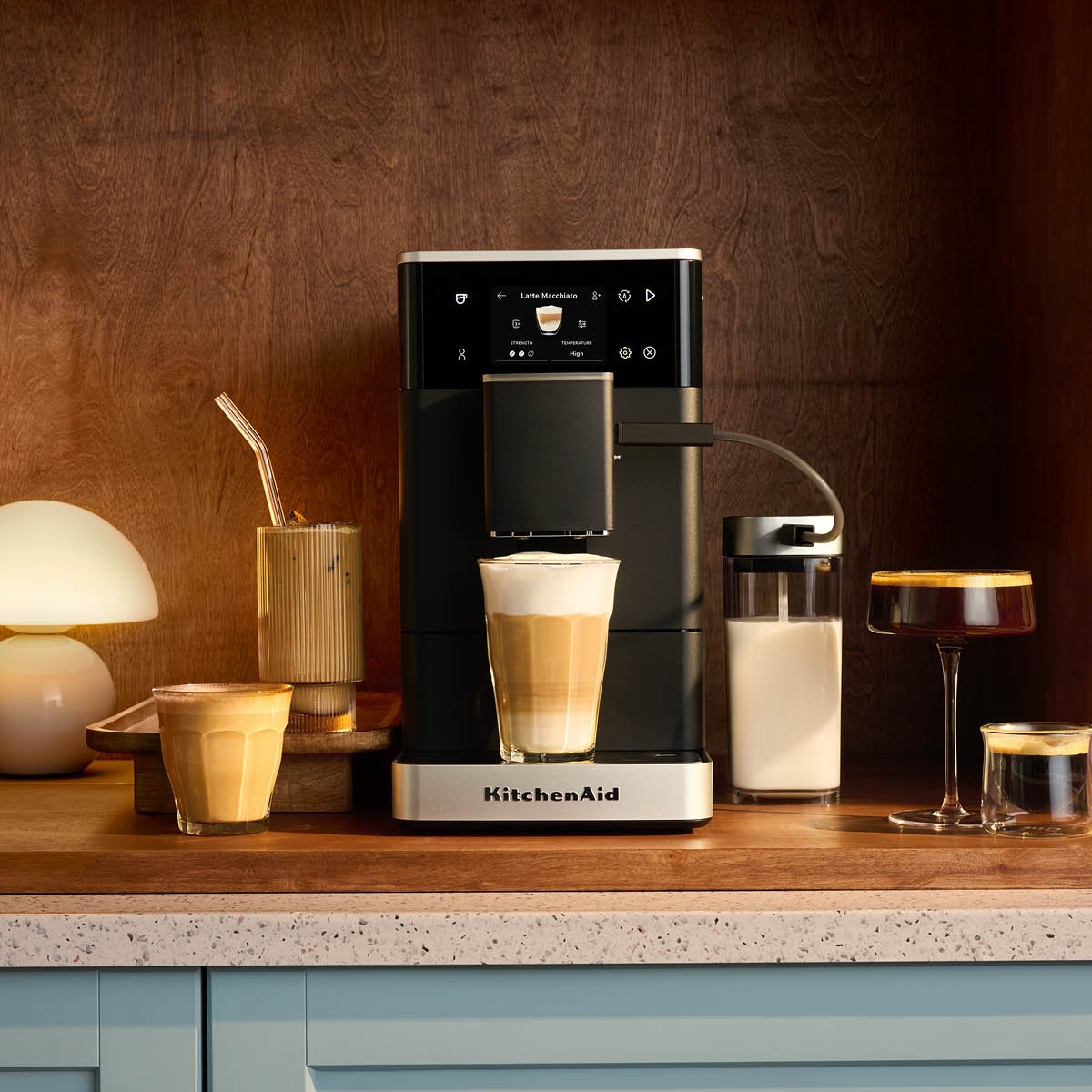 Elegant KitchenAid espressomaskin på köksbänk med flera olika kaffedrycker och mjölkkanna runtomkring.