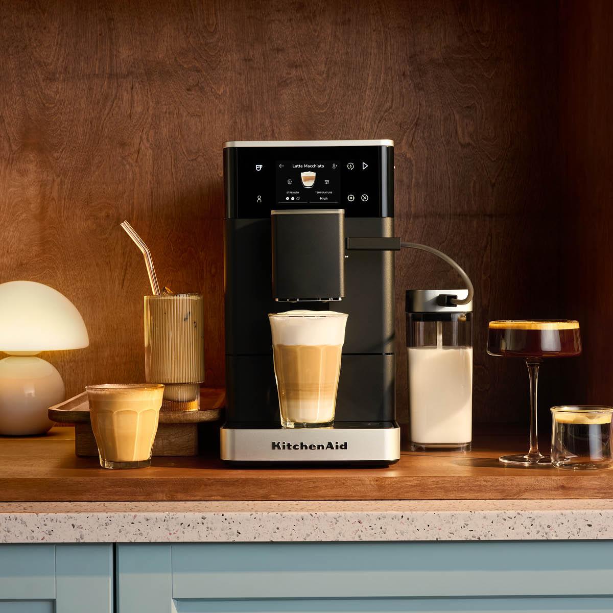Elegant KitchenAid espressomaskin på köksbänk med flera olika kaffedrycker och mjölkkanna runtomkring.