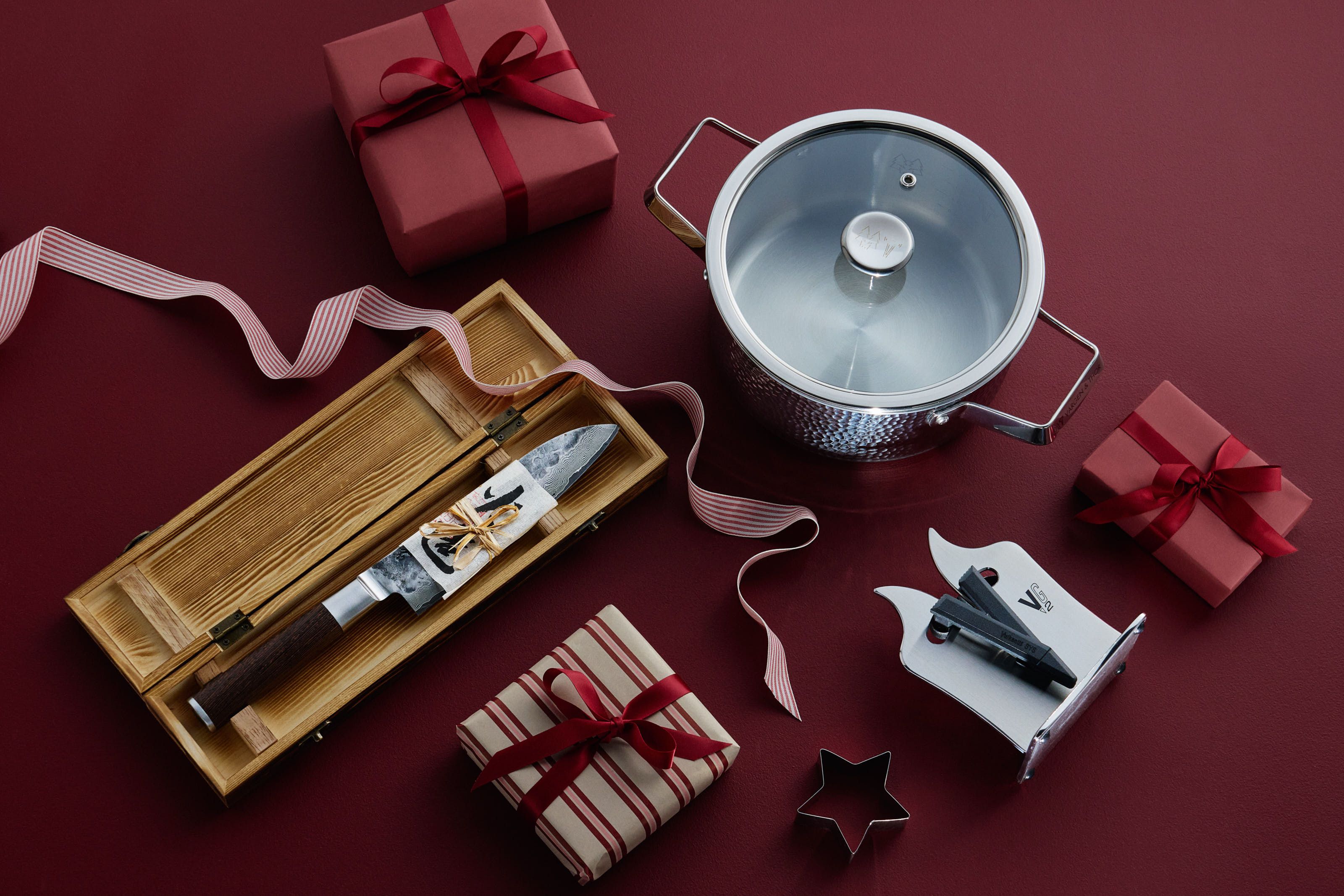 Köksgåvor, inklusive en kniv i en trälåda, en gryta och inslagna paket, på en röd yta.