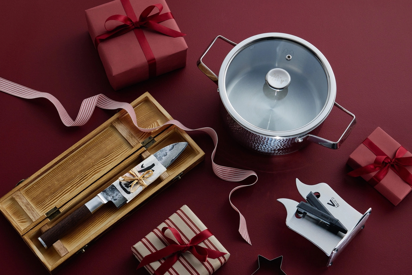 Köksgåvor, inklusive en kniv i en trälåda, en gryta och inslagna paket, på en röd yta.