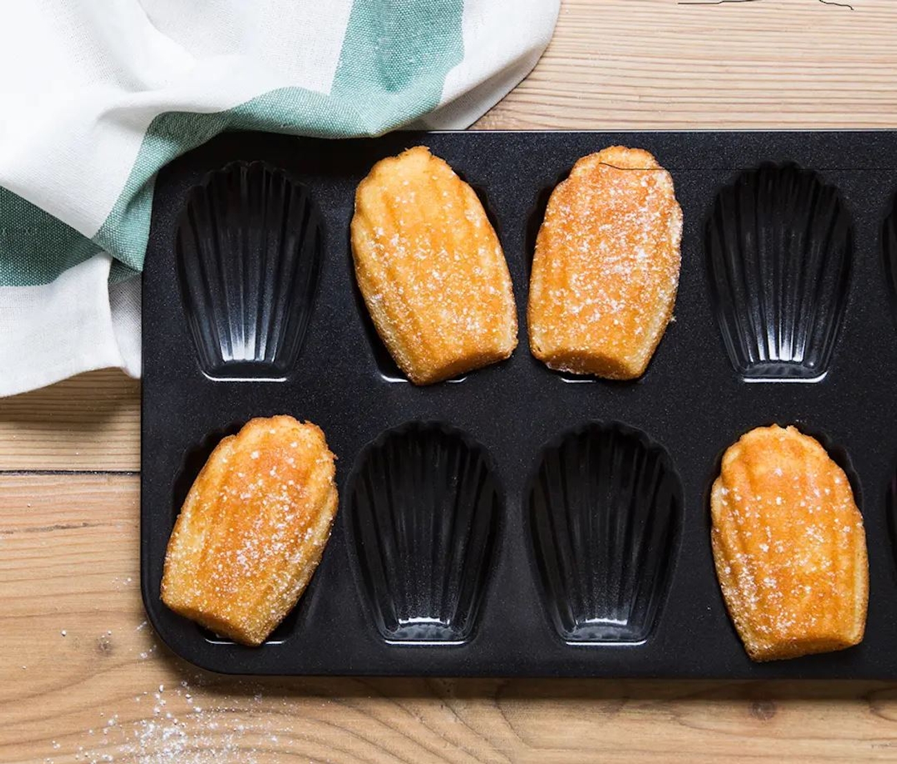 Madeleineformar med nygräddade Madeleinekakor på en köksbänk