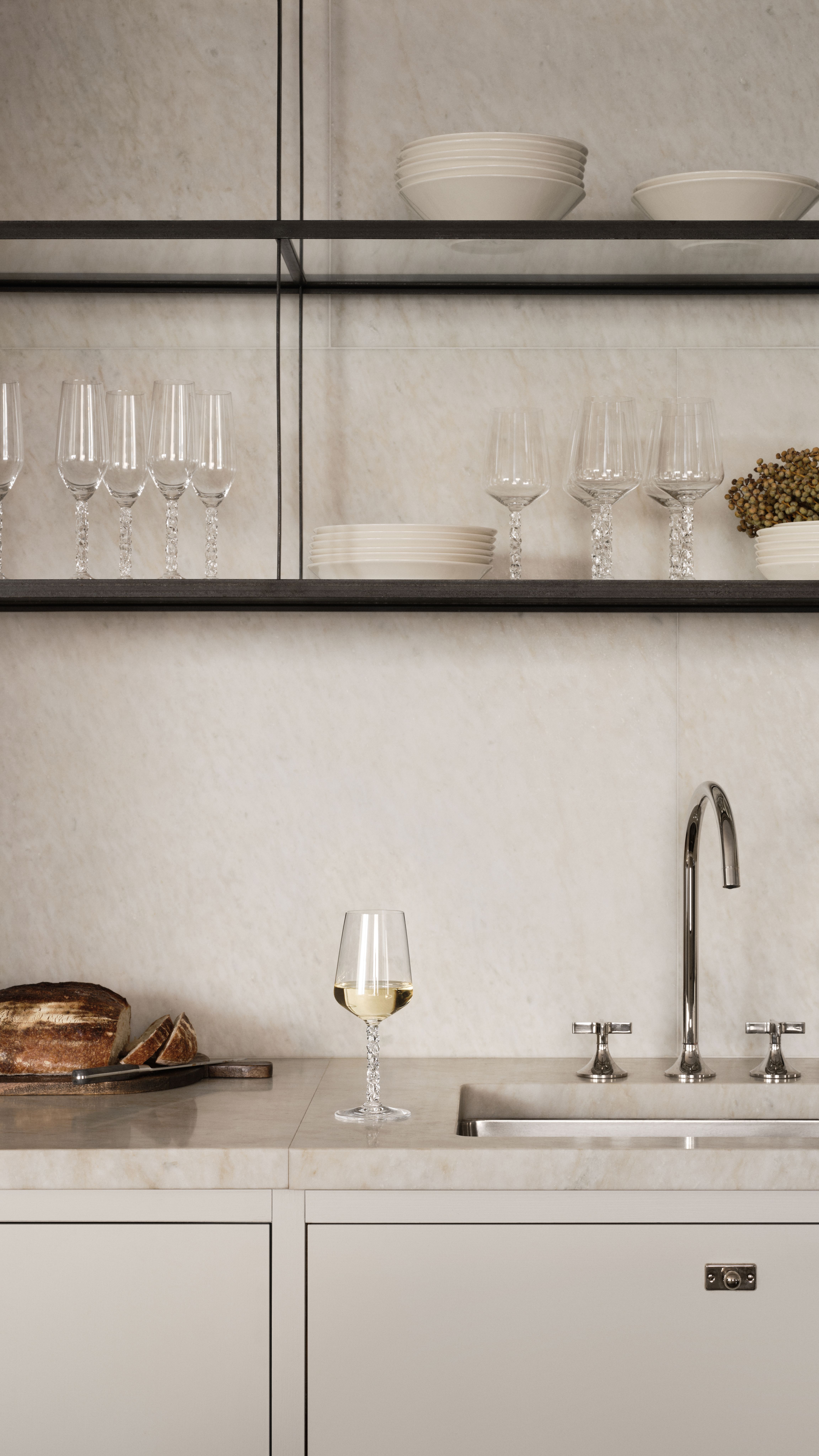 Elegant, minimalist köksbänk i marmor med vinglas, bröd och öppna hyllor med glas och porslin.