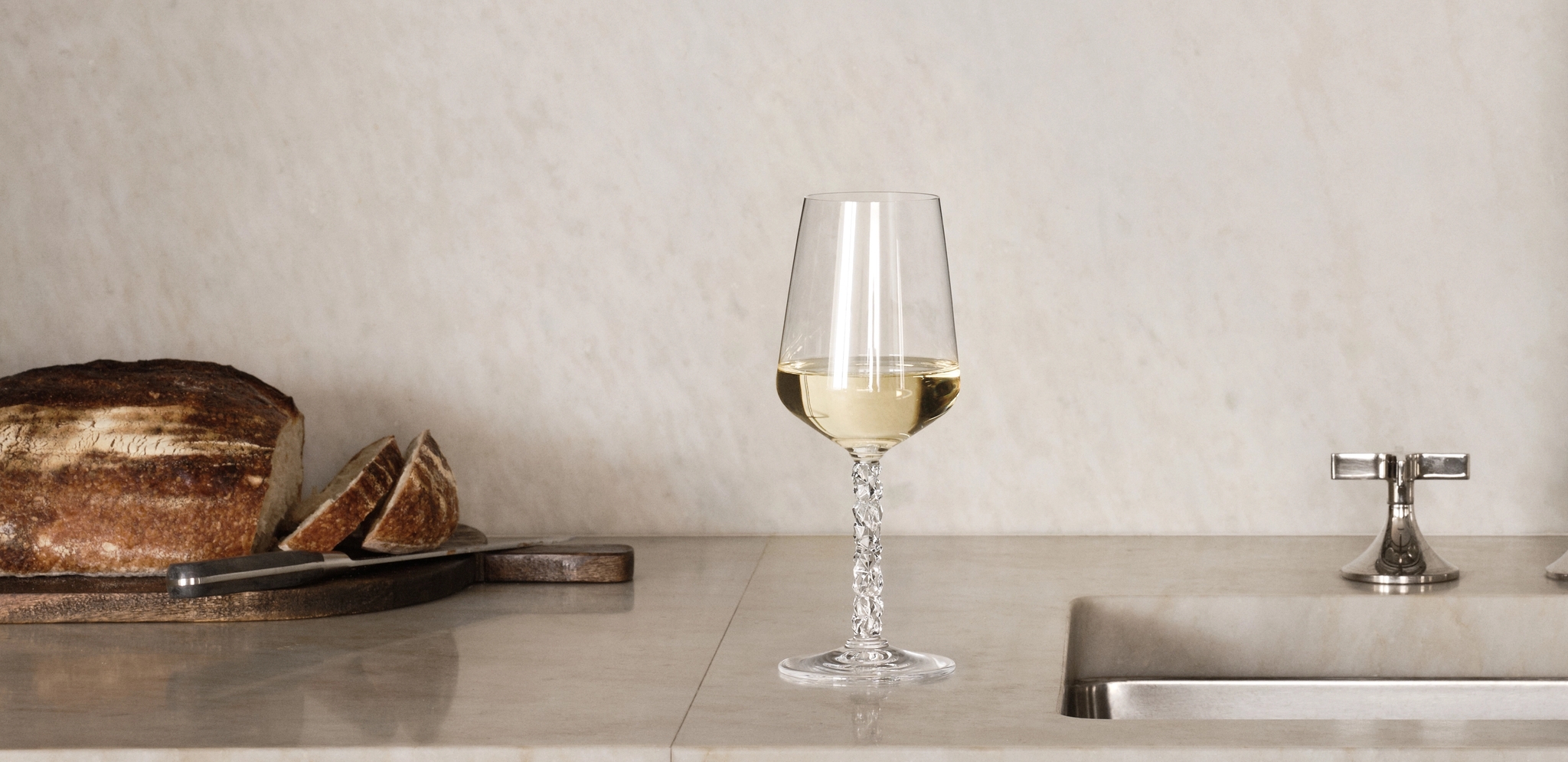 Elegant, minimalist köksbänk i marmor med vinglas, bröd och öppna hyllor med porslin och glas.