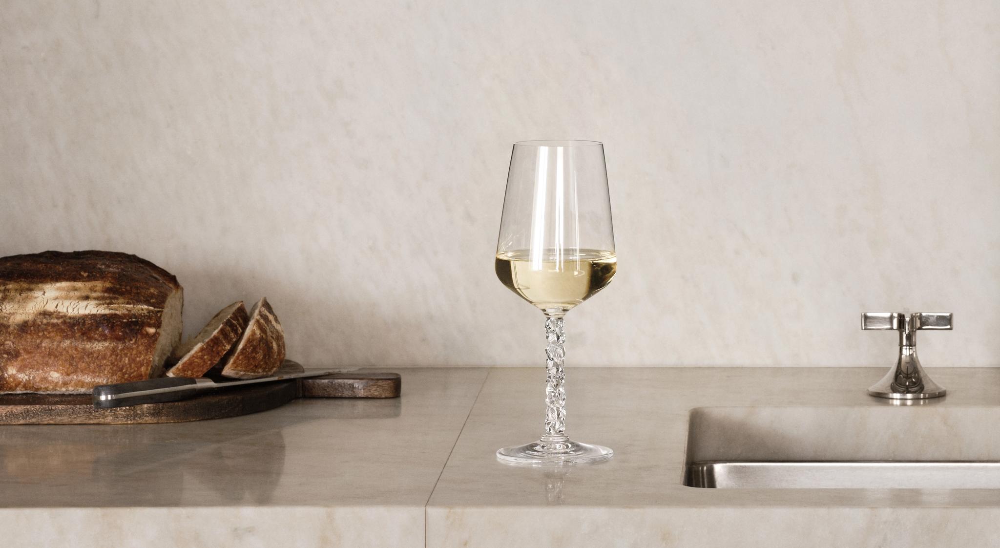 Elegant, minimalist köksbänk i marmor med vinglas, bröd och öppna hyllor med glas och porslin.