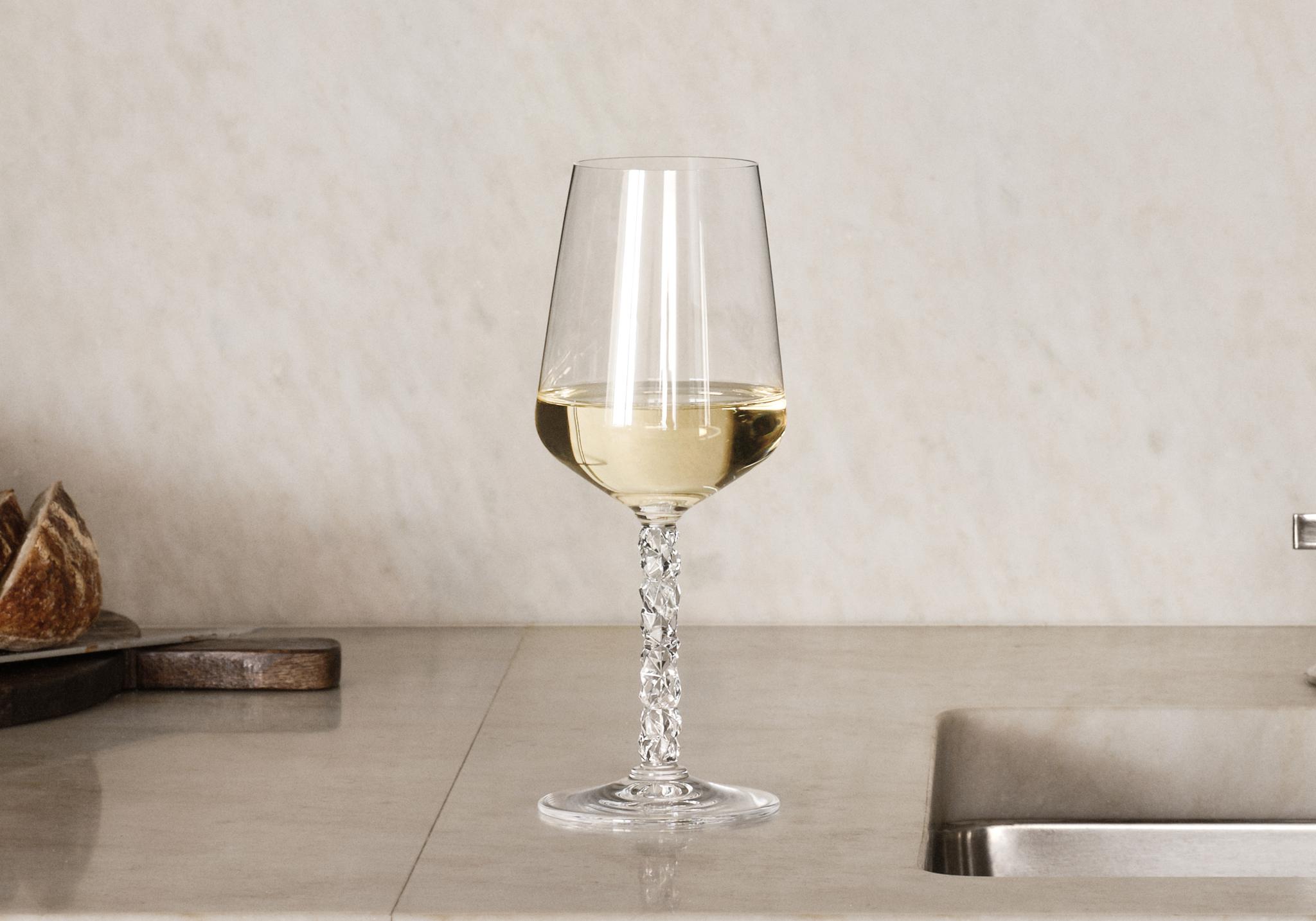 Elegant marmorkök med öppna hyllor, kristallglas, vitt porslin, bröd och ett glas vitt vin vid diskhon.