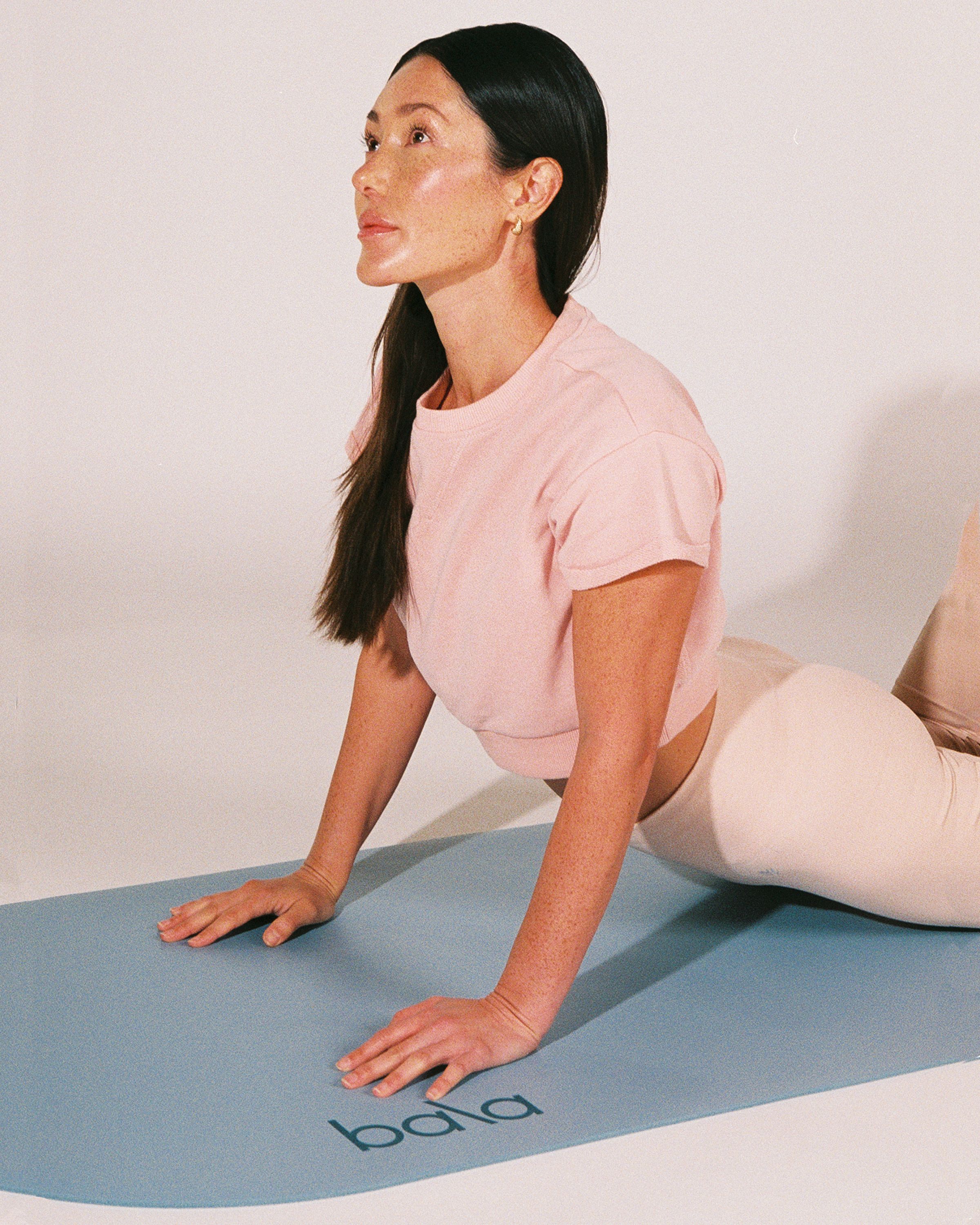 Kvinna gör en uppåtgående hund-yogaposition på en ljusblå Bala-yogamatta.