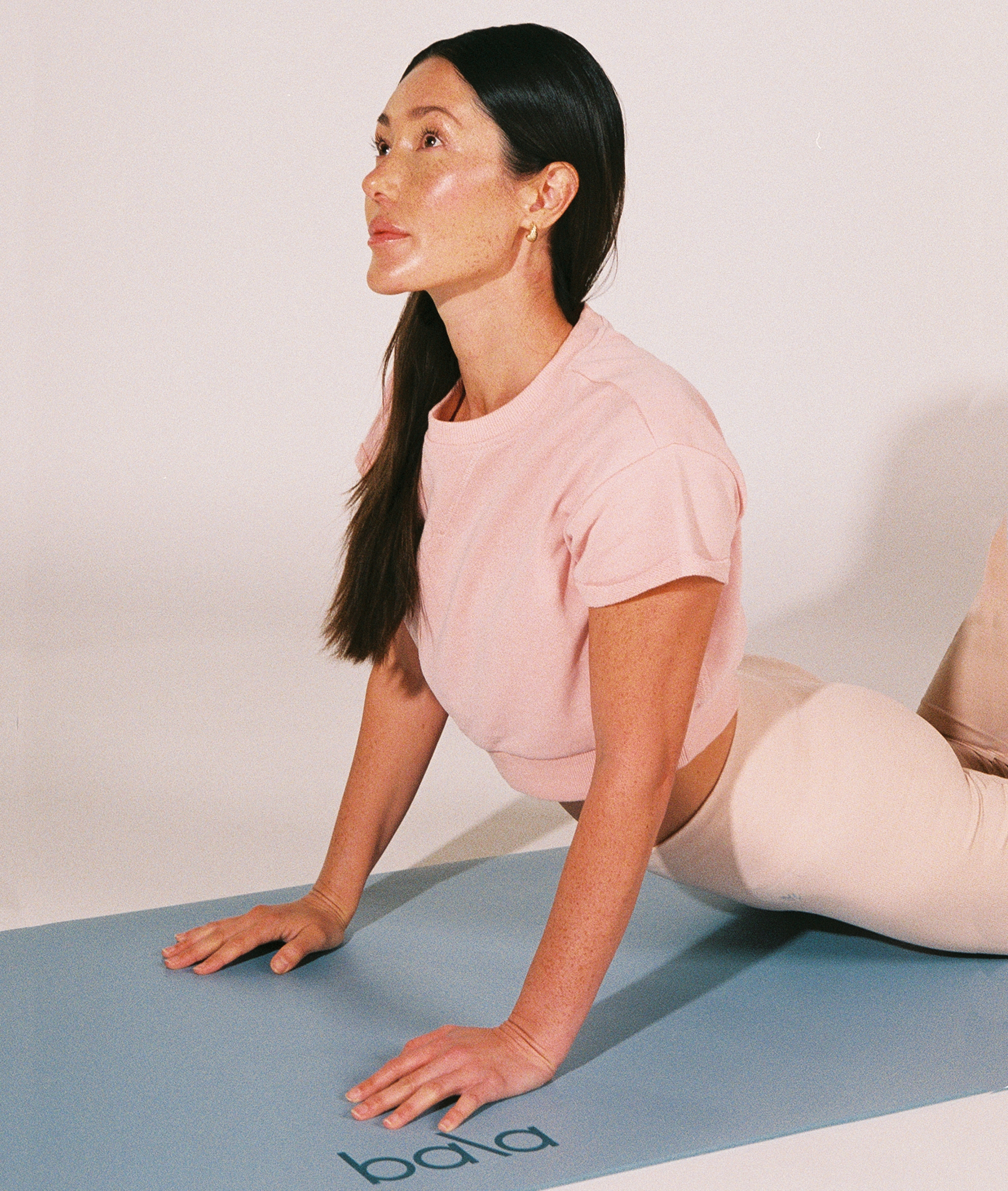 Kvinna gör en uppåtgående hund-yogaposition på en ljusblå Bala-yogamatta i studio.