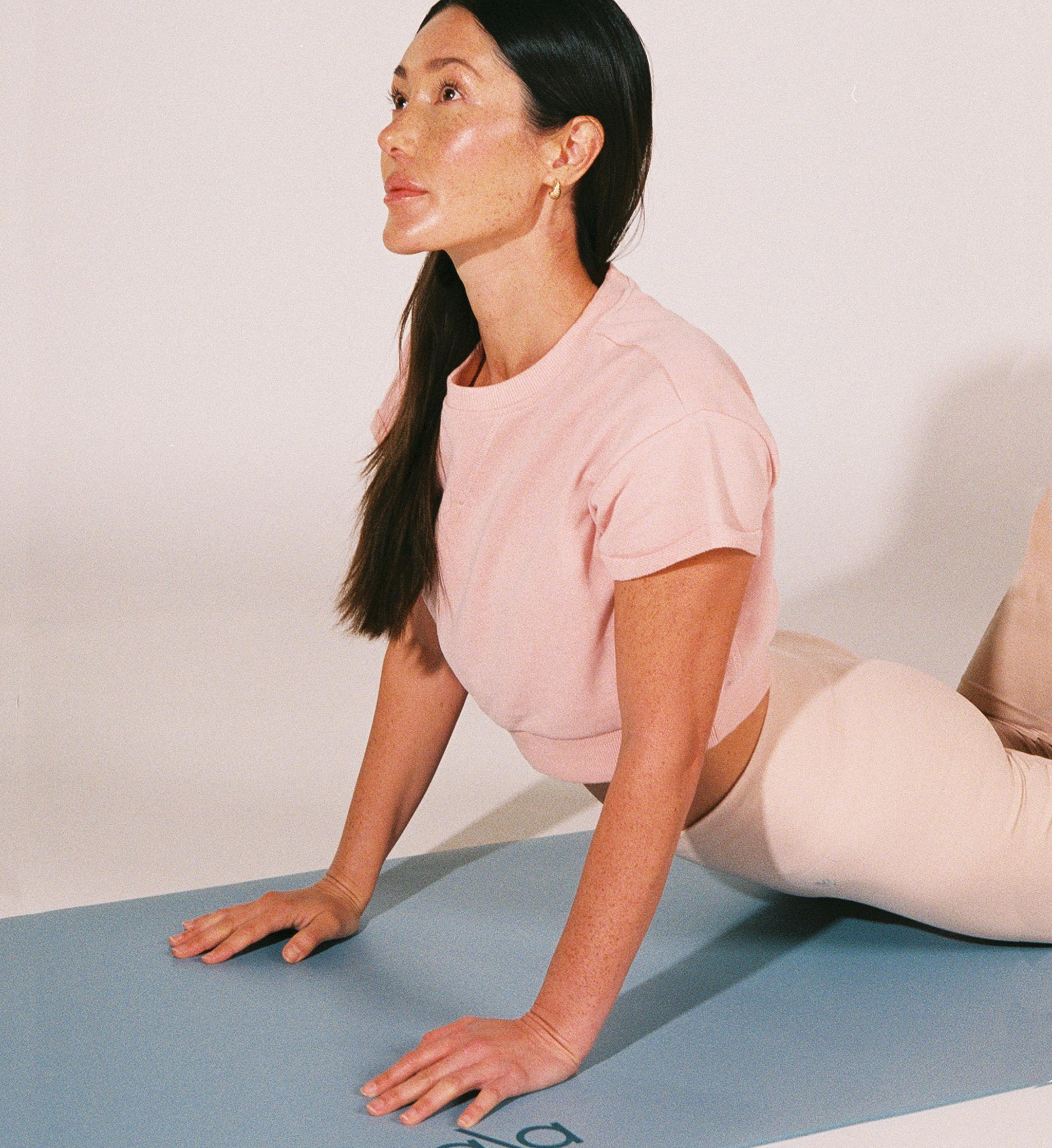 Kvinna gör en uppåtgående hund-yogaposition på en ljusblå Bala-yogamatta.
