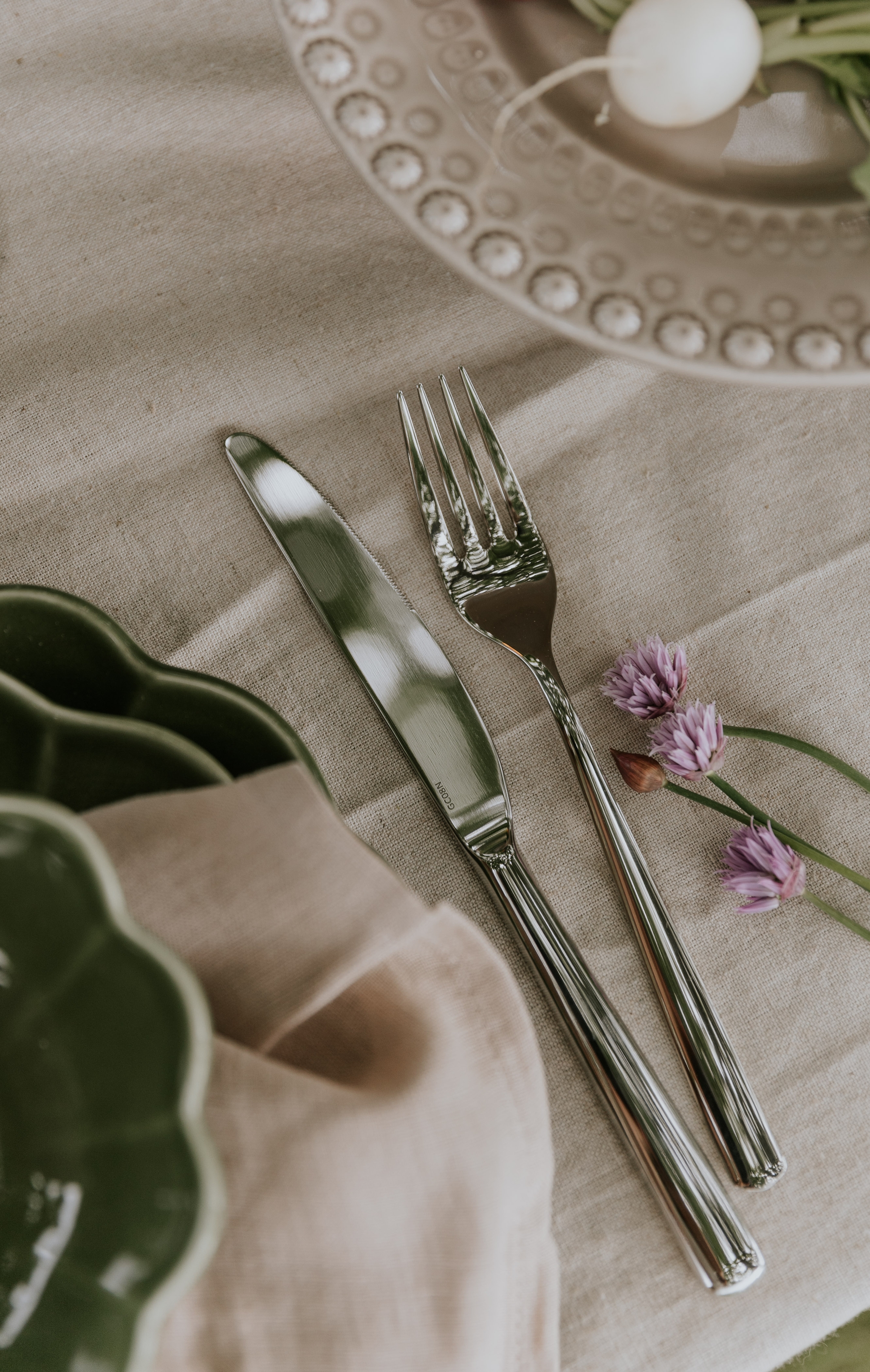 Matplats med fokus på bestick i silver liggandes på en beige bordsduk