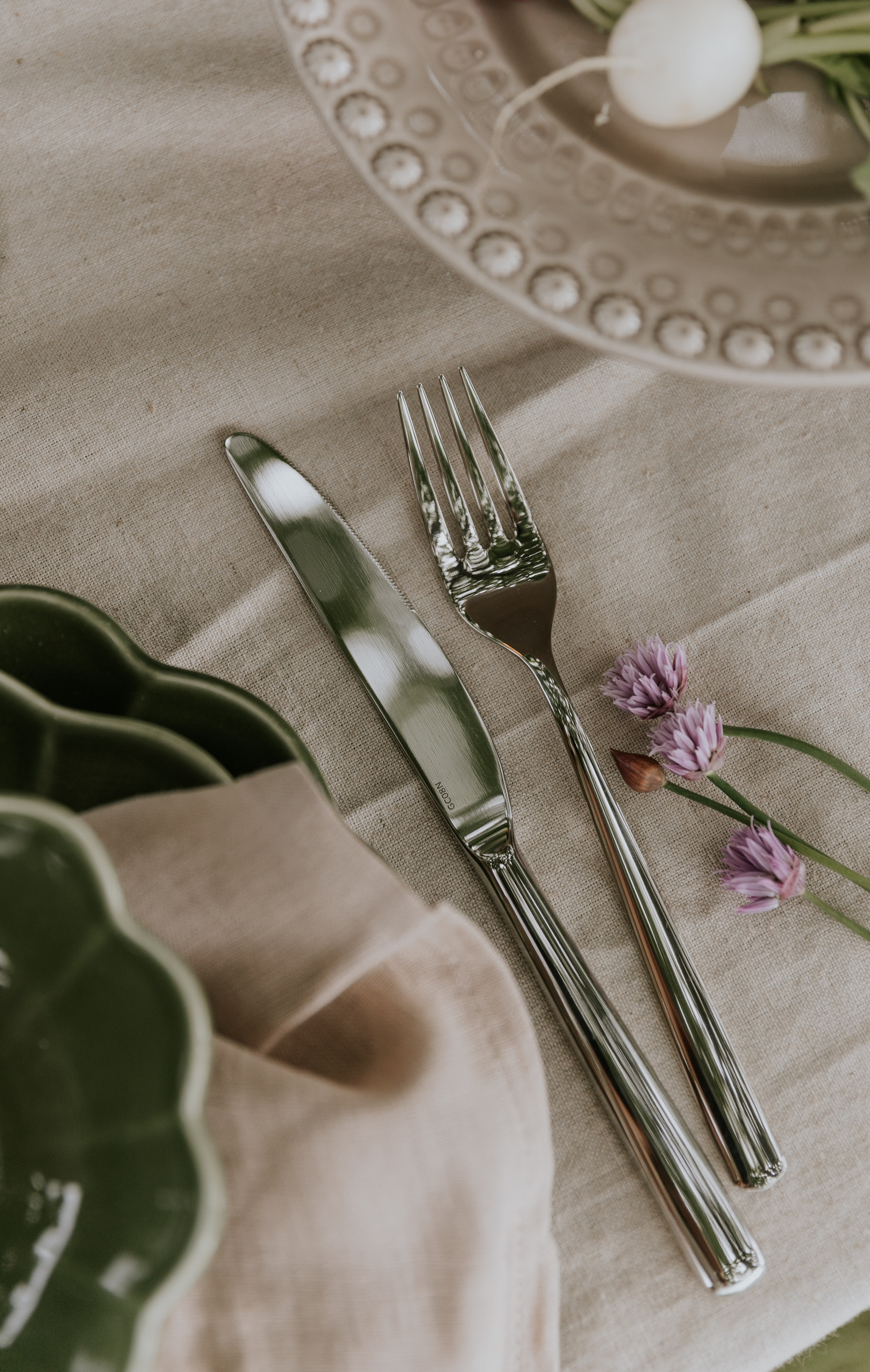 Matplats med fokus på bestick i silver liggandes på en beige bordsduk