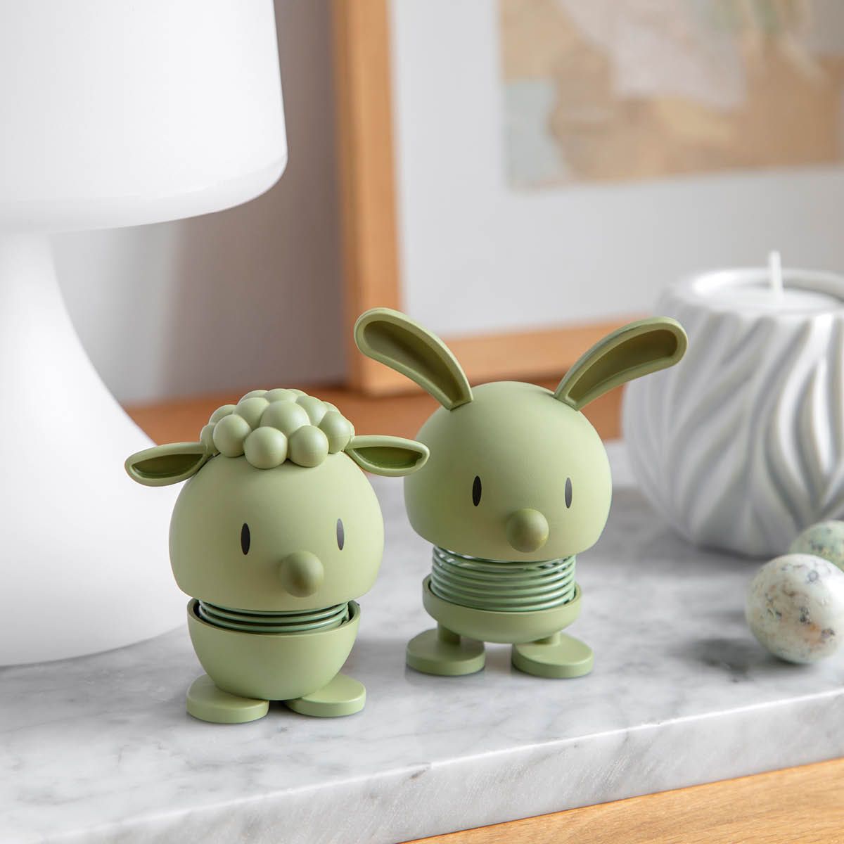 To lysegrønne fjærbelastede figurer, en sau og en kanin, på en marmorovertflate