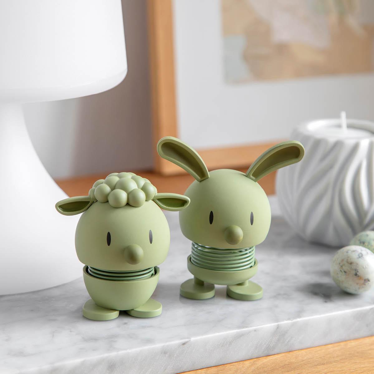 To lysegrønne fjærbelastede figurer, en sau og en kanin, på en marmorovertflate