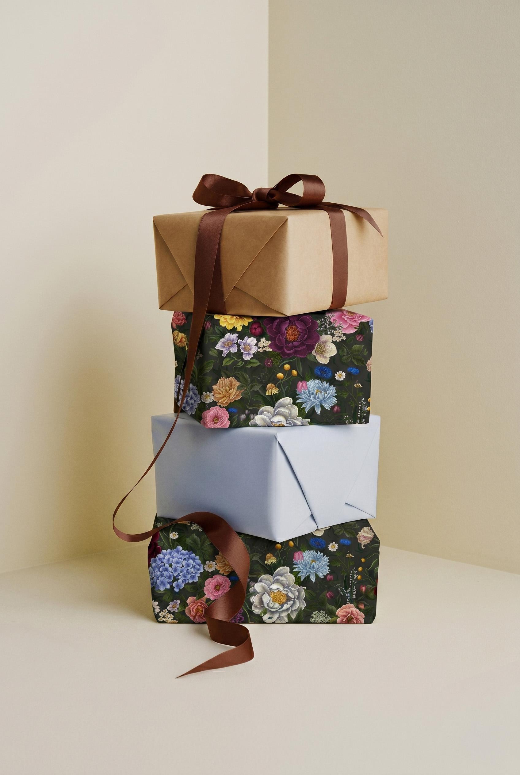 En stapel elegant inslagna paket med blommigt presentpapper och brunt sidenband står mot en ljus beige bakgrund.