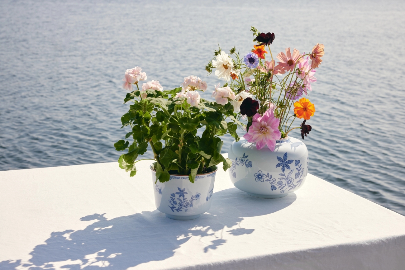 Två stora vaser i vit färg med blåa blommor på sig, på ett bord vid vattnet