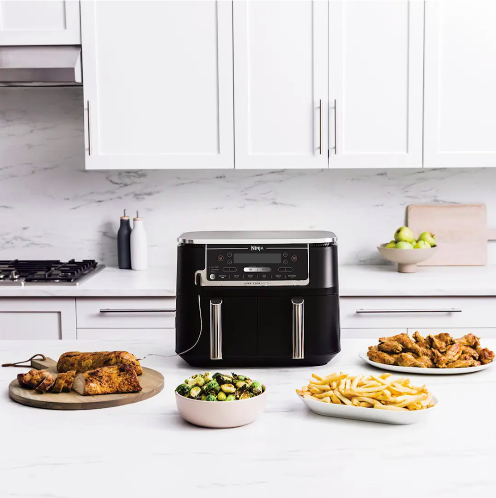 A black Ninja air fryer on a kitchen counter with cooked chicken, brussels sprouts, french fries, and chicken wings.