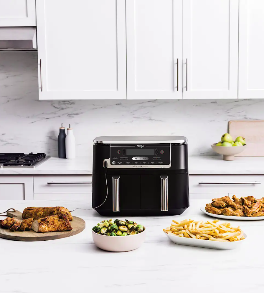A black Ninja air fryer on a kitchen counter with cooked chicken, brussels sprouts, french fries, and chicken wings.