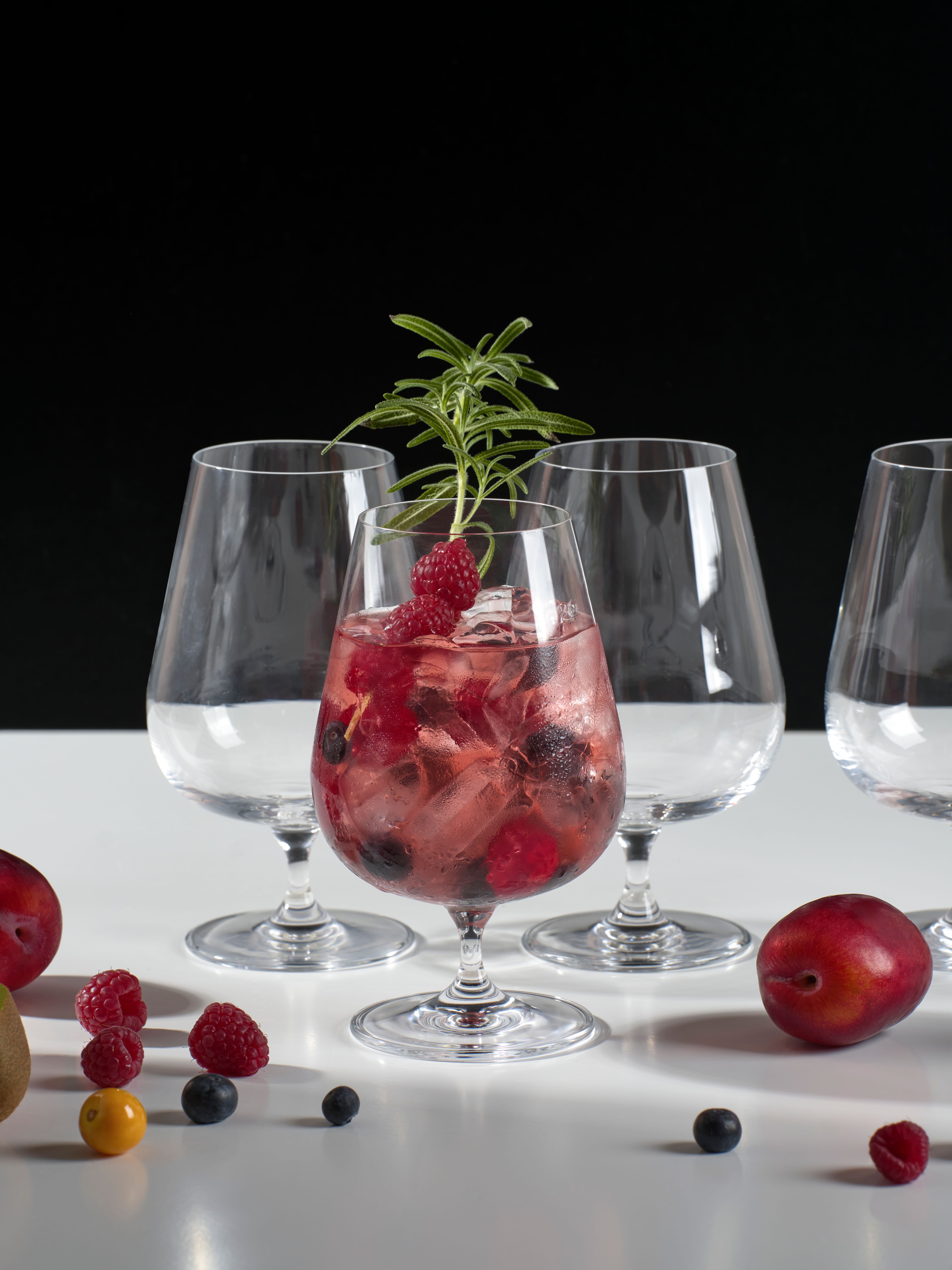 Rosa cocktail med isbiter, friske bær og rosmarin i et elegant glass.