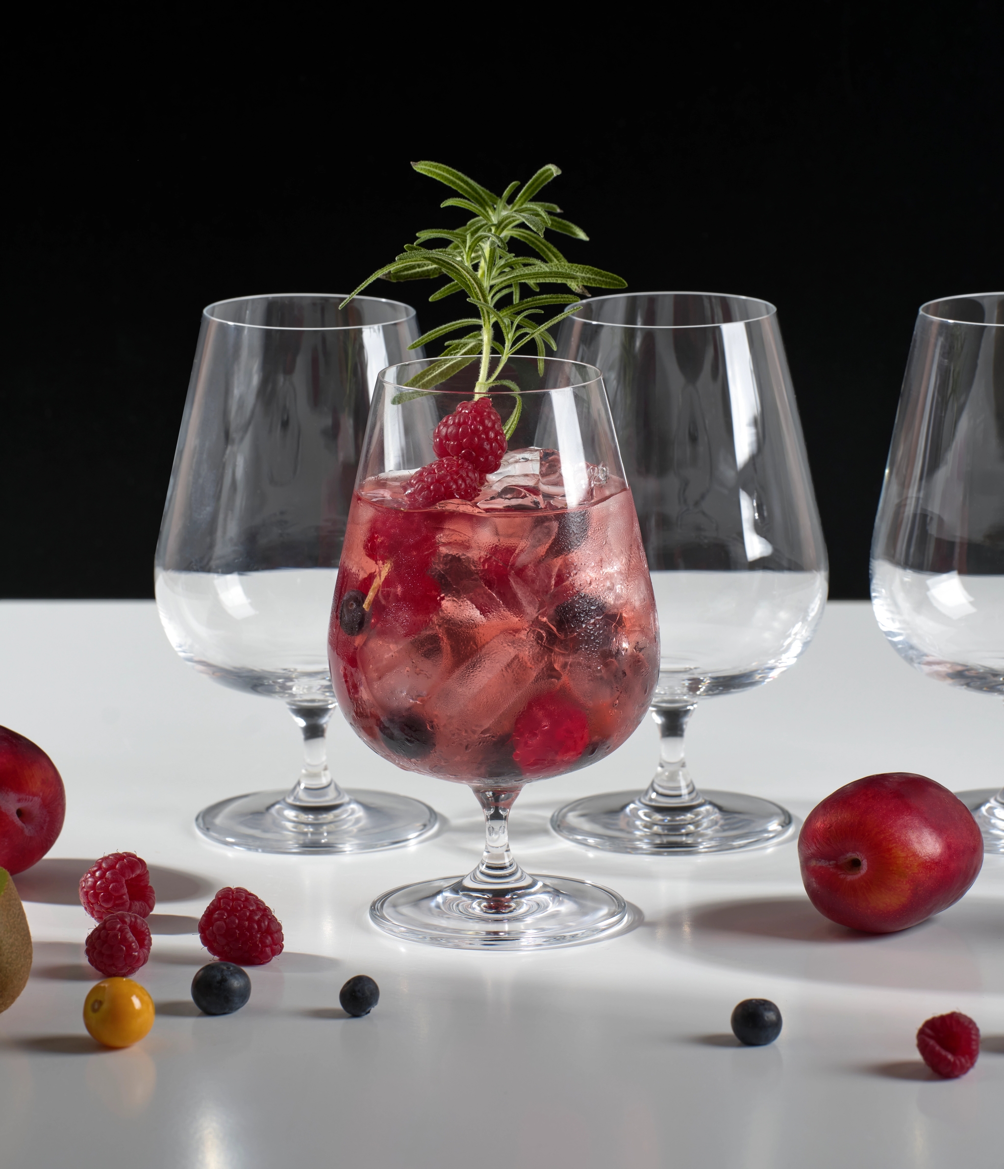 Rosa cocktail med isbiter, friske bær og rosmarin i et elegant glass.