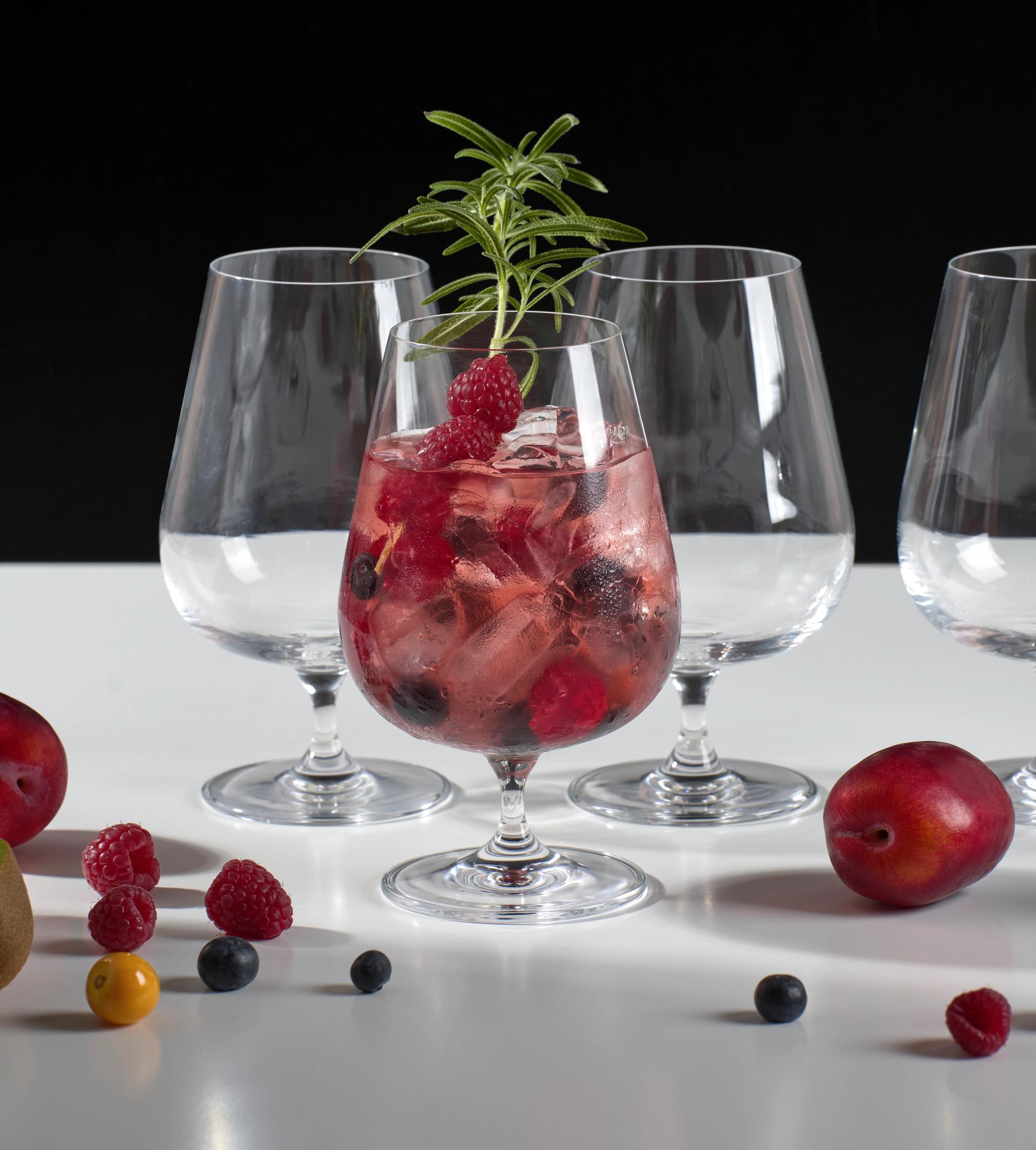 Rosa cocktail med isbiter, friske bær og rosmarin i et elegant glass.