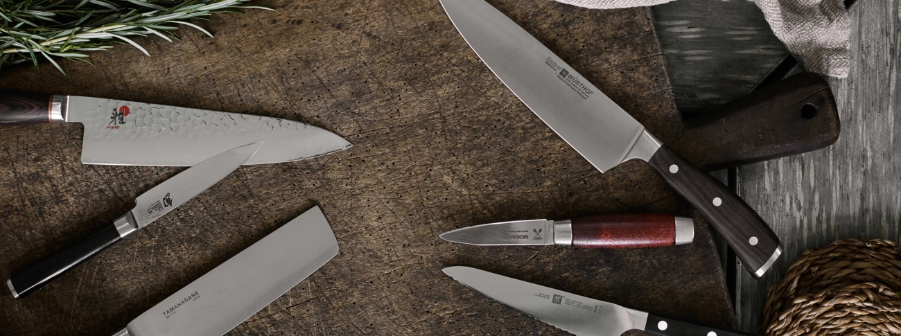 Zwilling knivar i olika storlekar och modeller liggandes på en träskärbräda