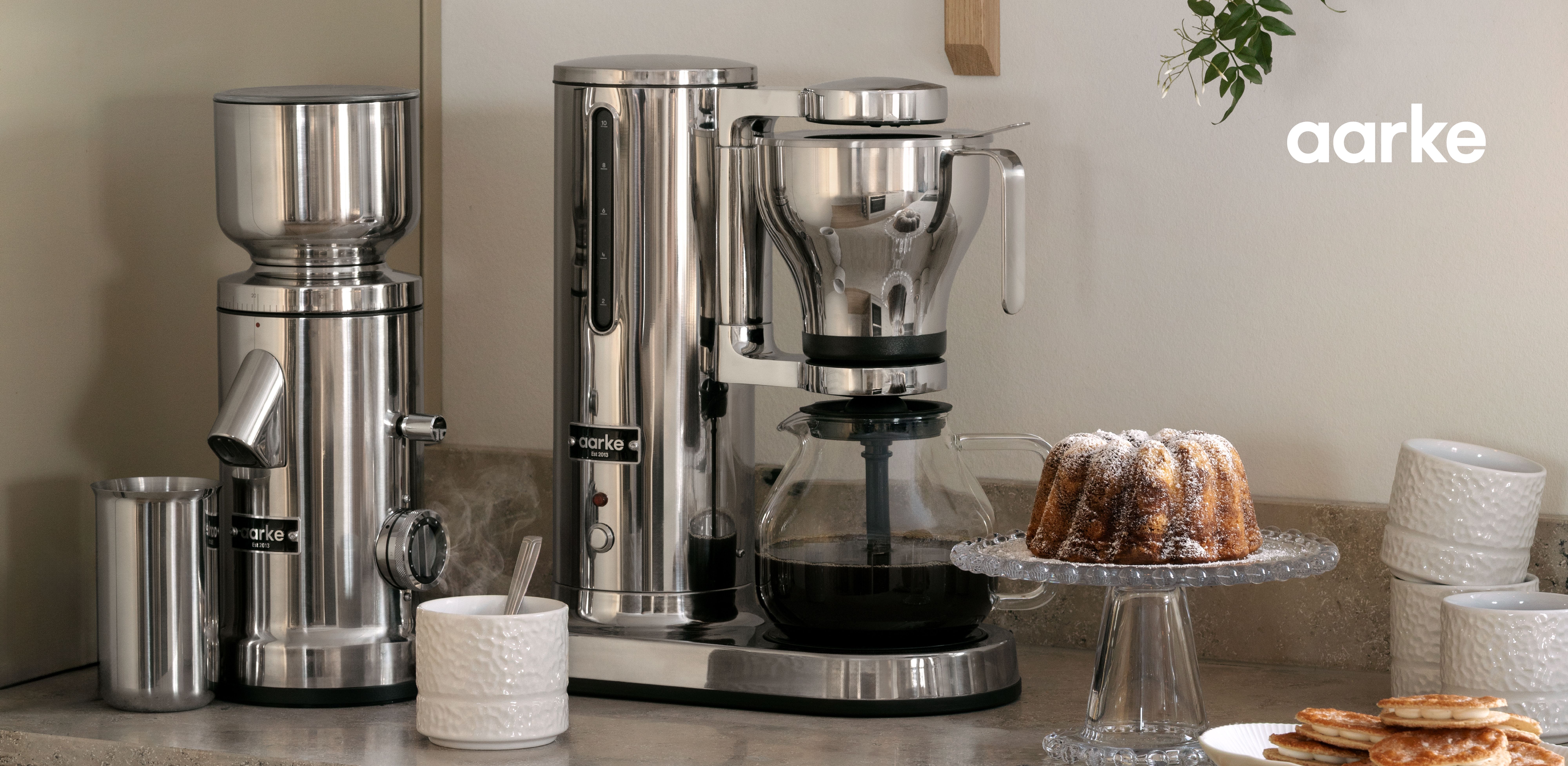 Aarke kaffekvarn och kaffebryggare i rostfritt stål på en köksbänk med en bundtkaka och pannkakor.