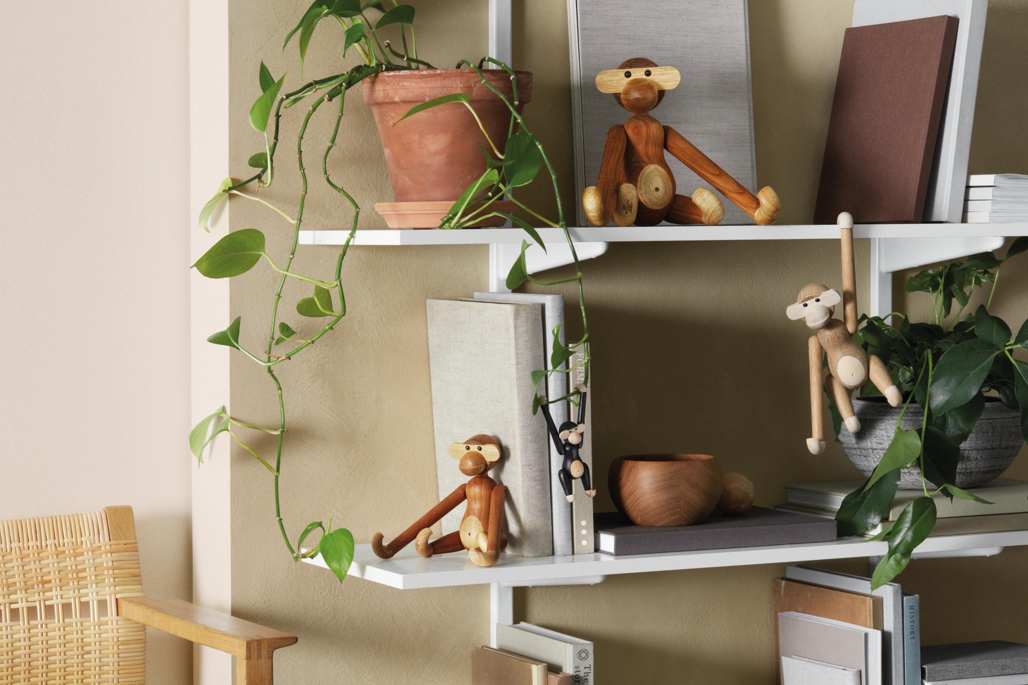 a shelf with monkeys , books , potted plants and a chair .
