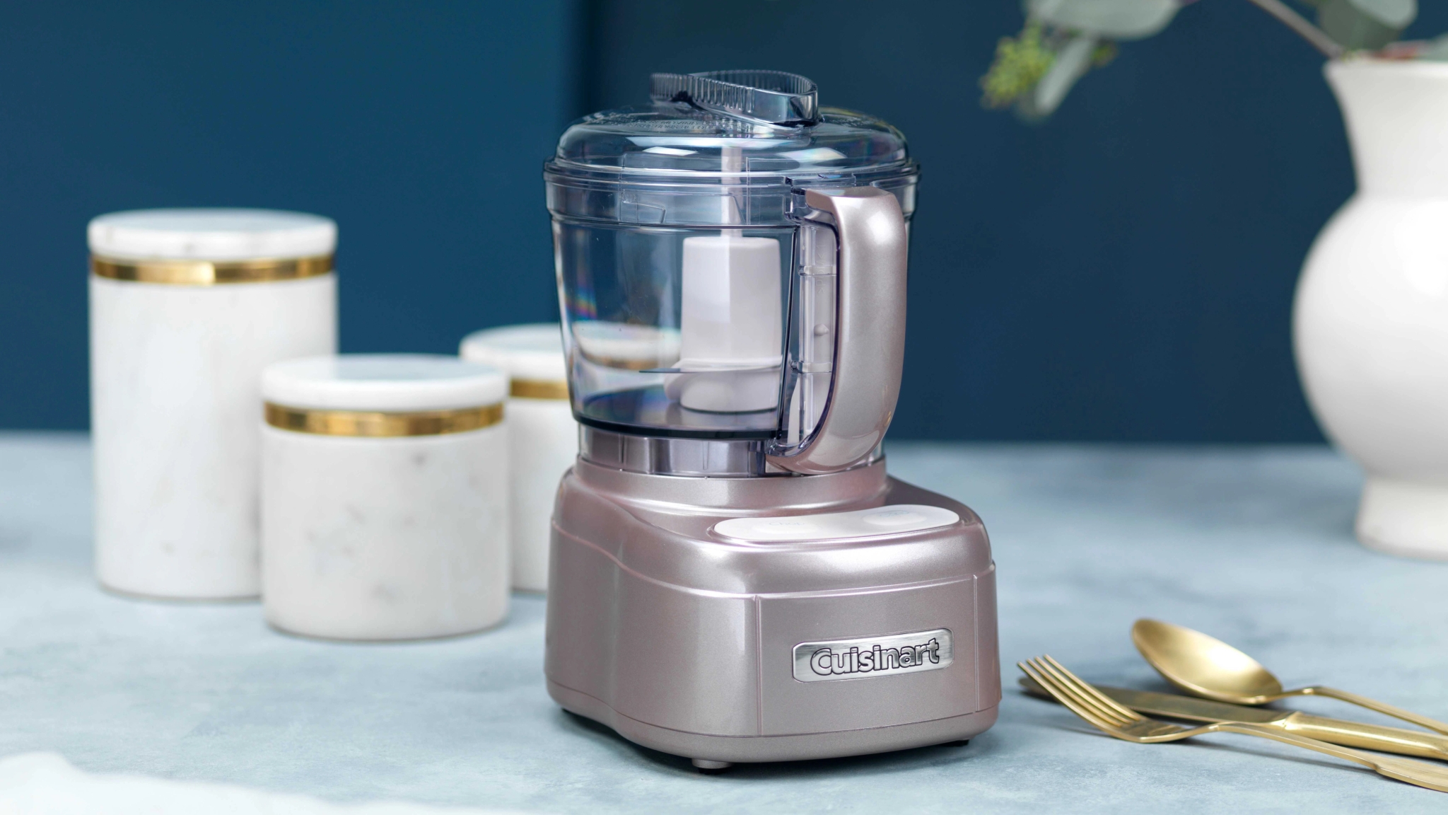 Cuisinart-monitoimikone keittiön tasolla kultaisilla aterimilla ja purkeilla taustalla.