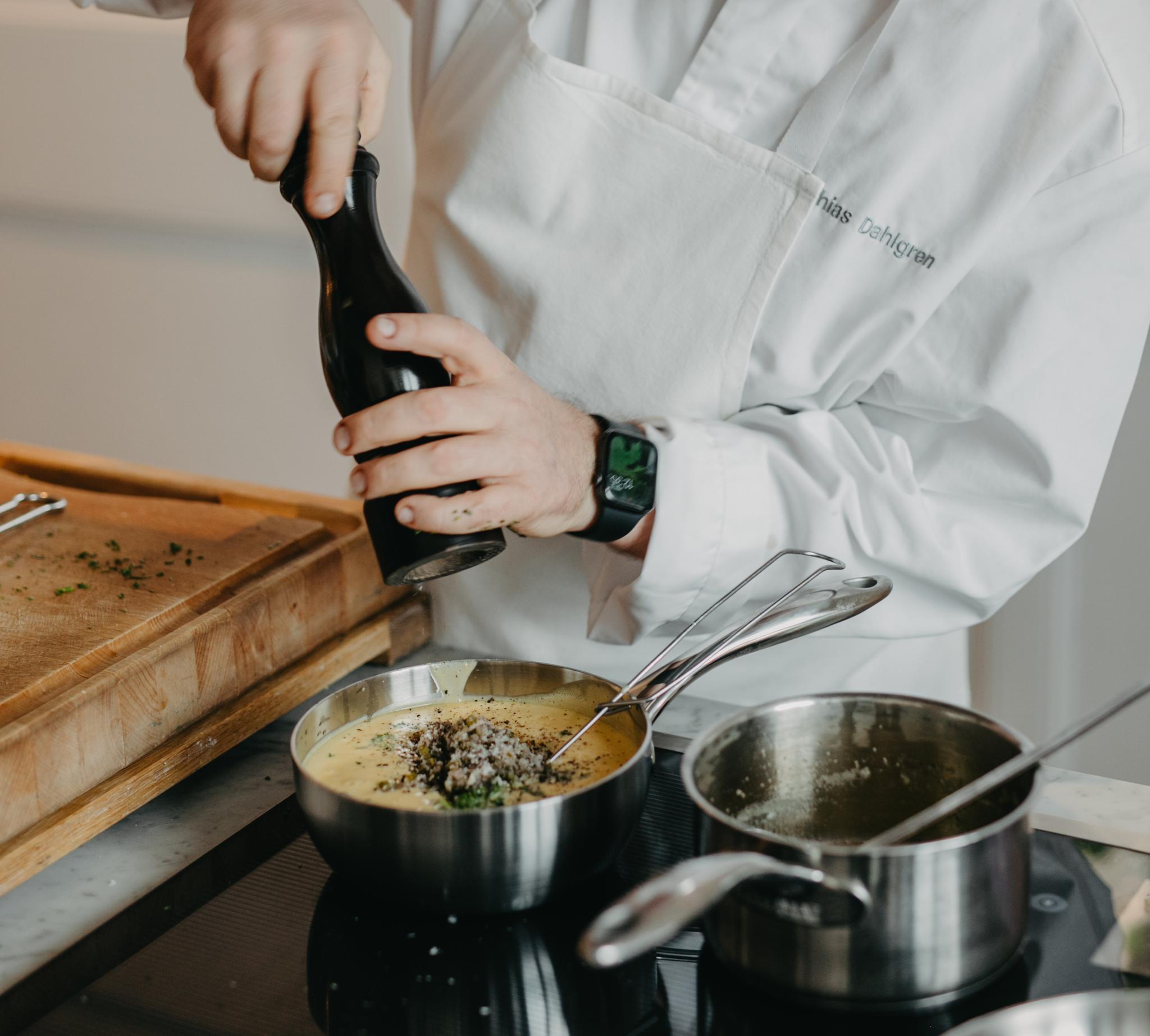 Kocken Mathias Dahlgren maler en pepparkvarn i en gryta på spisen.