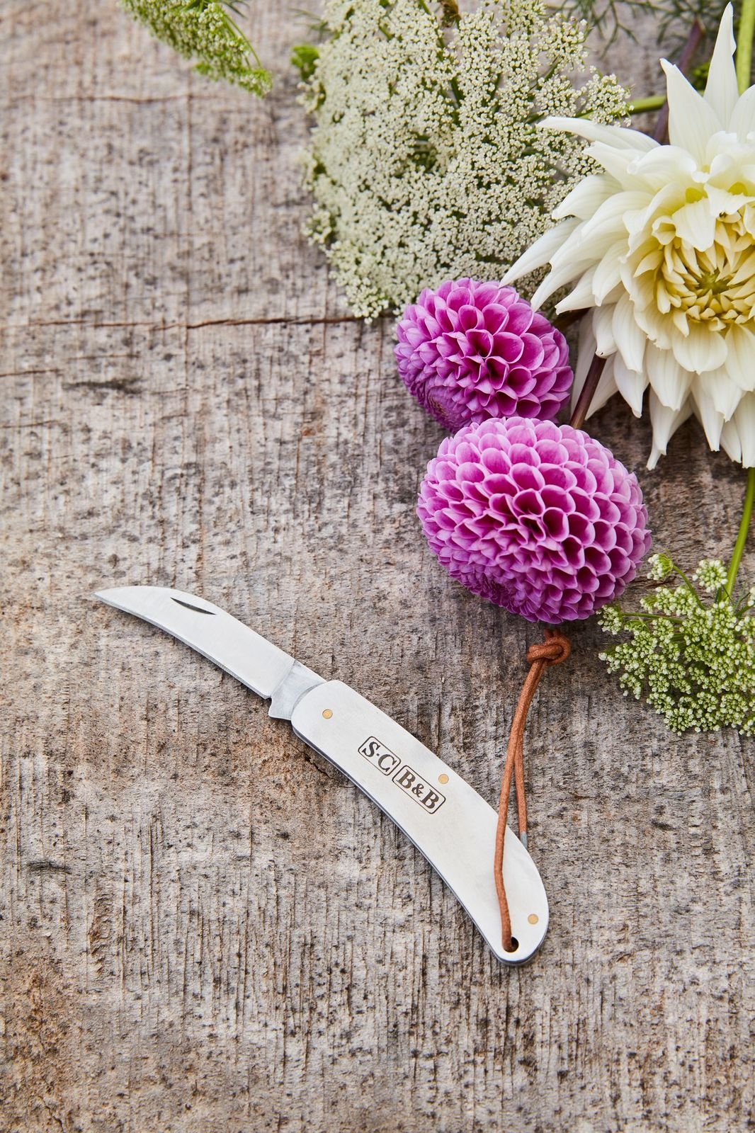 Fickkniv på träbänk med lila blommor