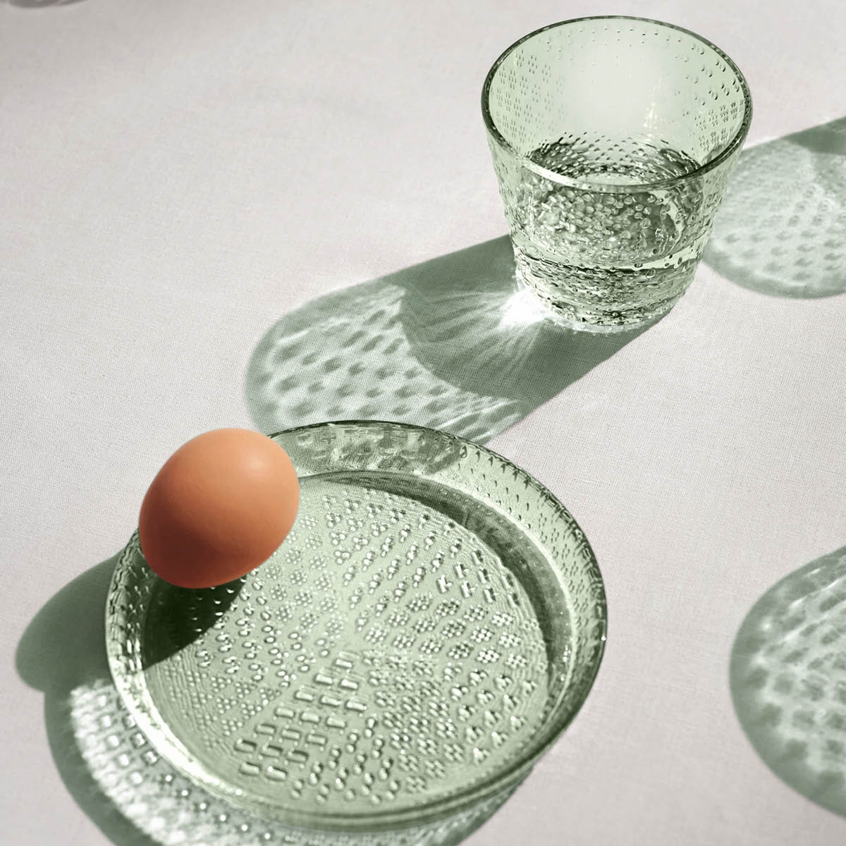 Tallrikar med hög kant i ljusgrönt glas med ett ägg liggandes på tallriken