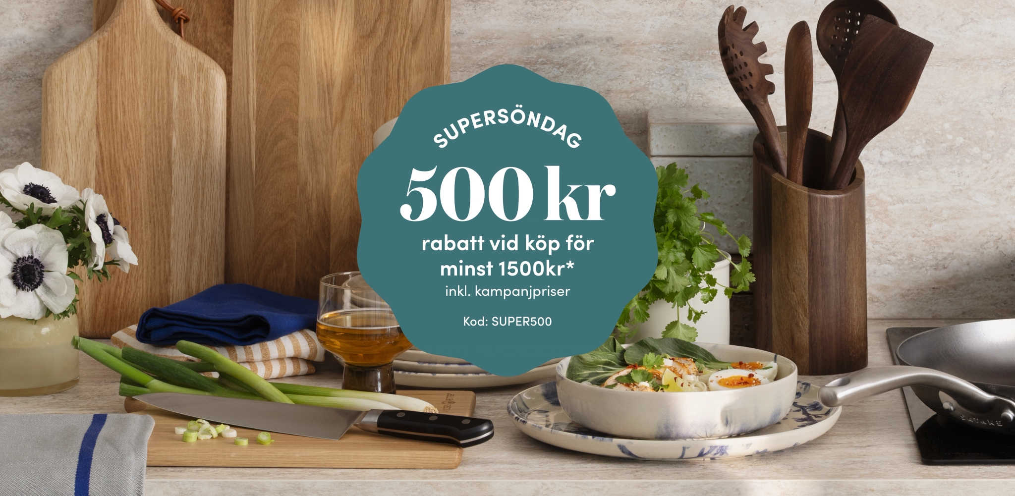 Köksscen med matlagningsingredienser och en framträdande blågrön banderoll för "Supersöndag" som erbjuder 500 kr rabatt på köp över 1500 kr med koden SUPER500.