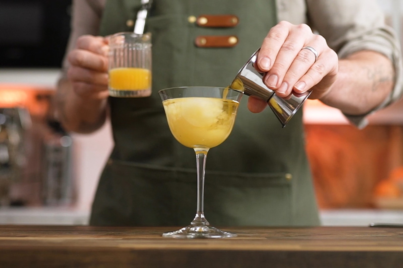 Mann med forkle blander en drink med drinkmål