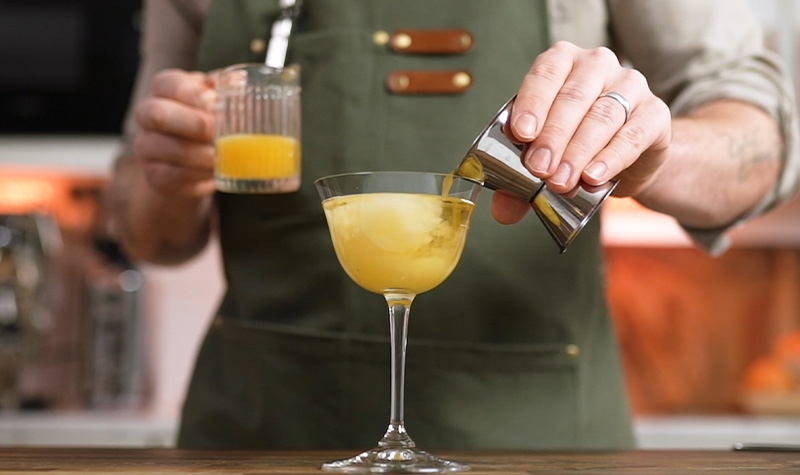 Man med förkläde blandar en drink med drinkmått