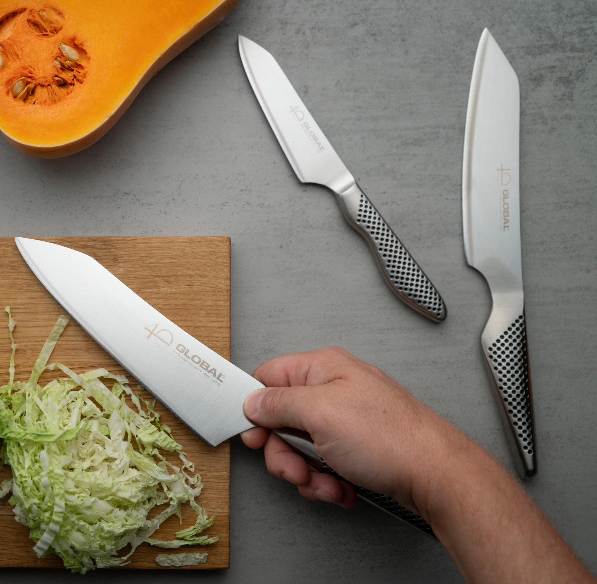 Hands chopping napa cabbage with a Global knife on a cutting board, with a halved butternut squash and other Global knives nearby.