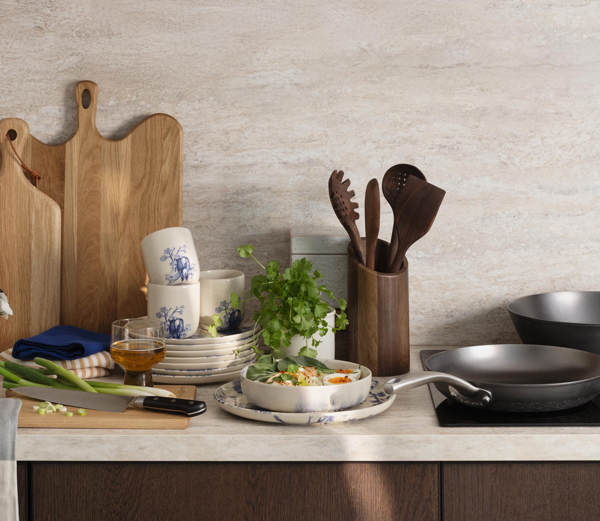 En köksbänk med en färdiglagad måltid, köksredskap, tallrikar och skärbrädor i trä.