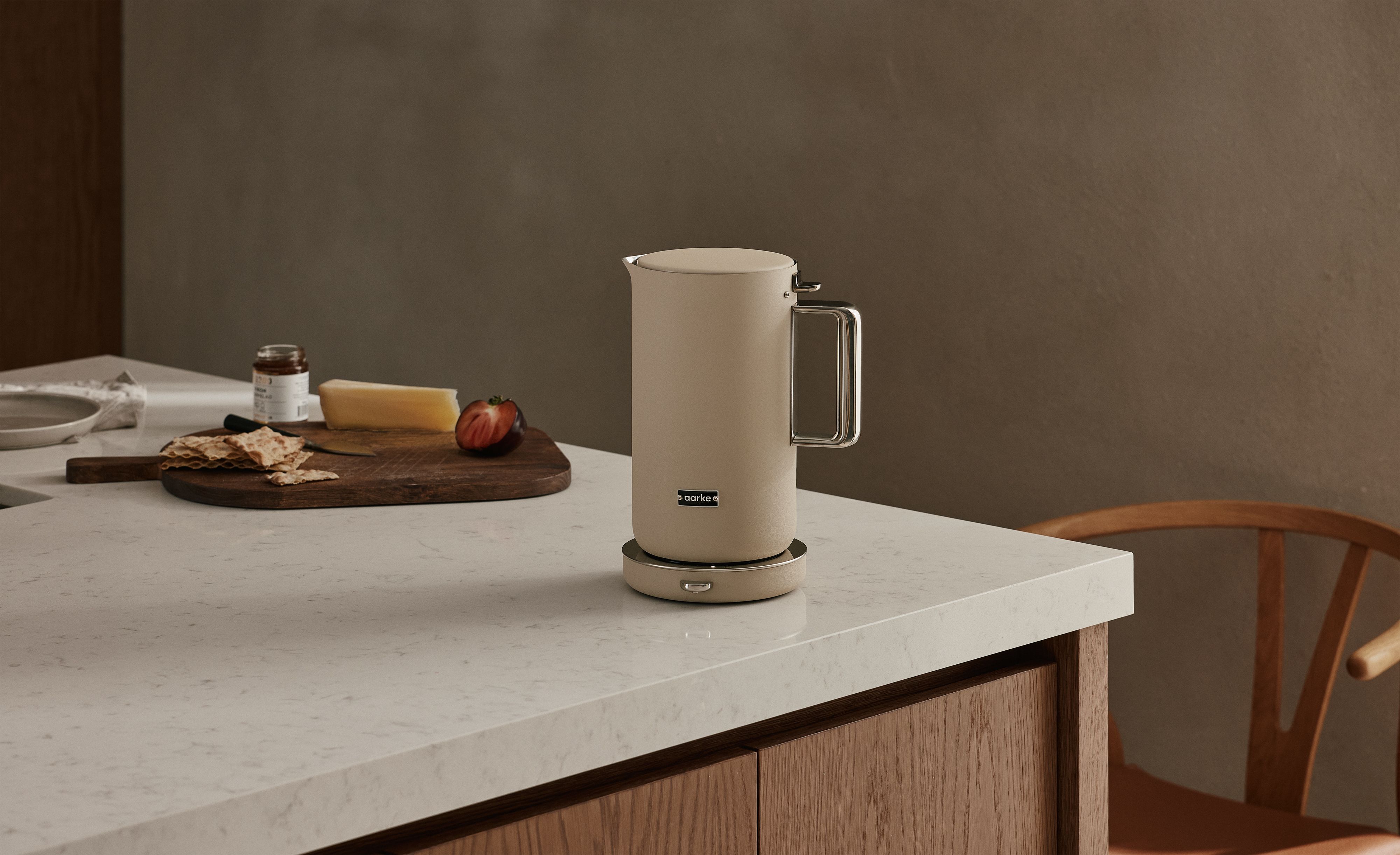 En beige vattenkokare står på en köksbänk bredvid en skärbräda med ost och kex.