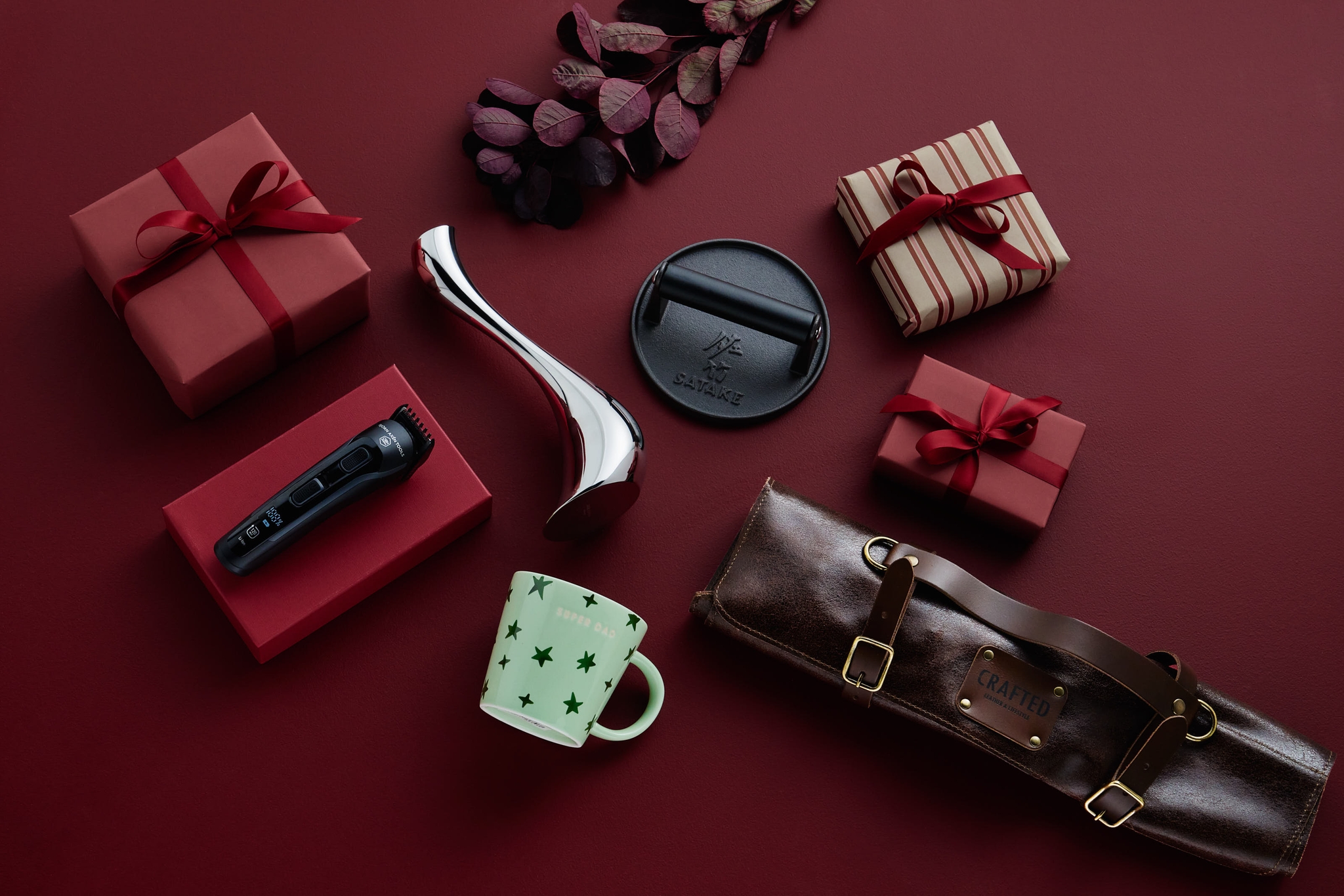 A collection of gifts including a shaver, grill press, mug, and wrapped boxes on a red background.