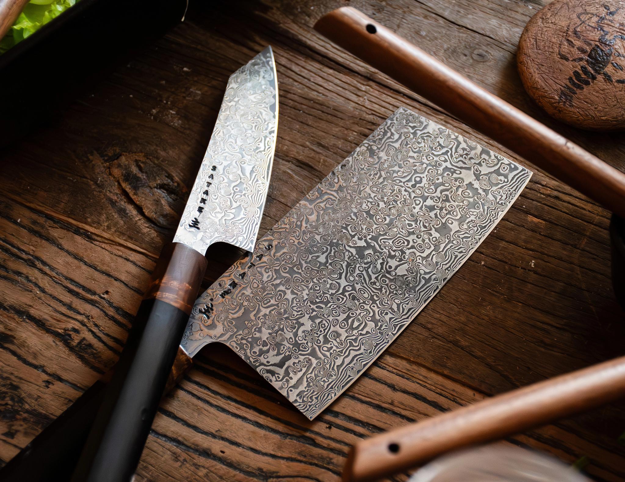 Kockkniv och köttyxa i damaskusstål på ett träbord.