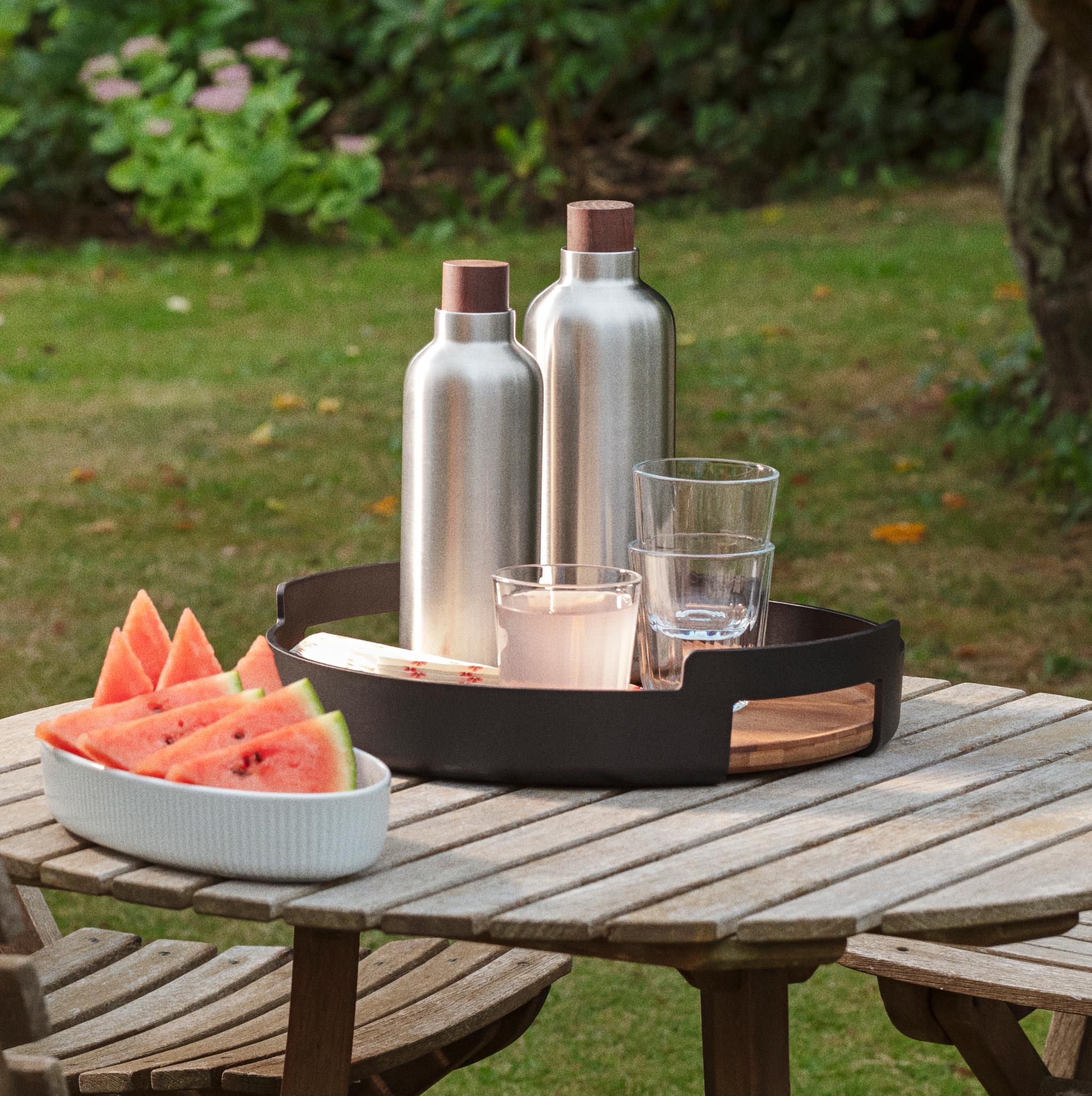 Vannmelon, to sølvfargede flasker og glass på et trebord i en hage