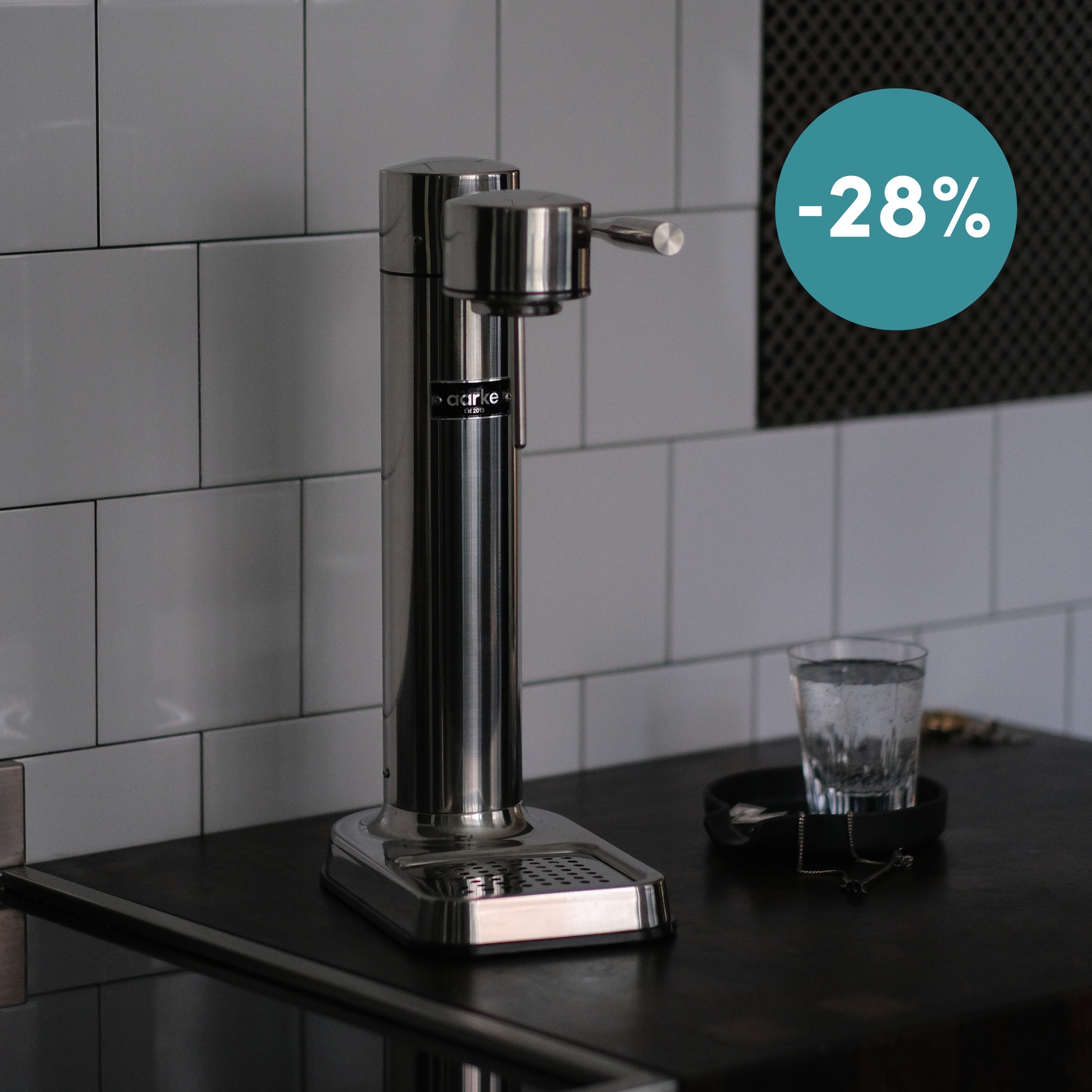 Henkilö valmistaa kuplivaa vettä mustalla Aarke-hiilihapottimella, lasi jäätä lähellä.