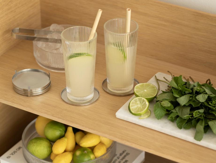 Lemonadstation på en trähylla med lime, färsk mynta och räfflade glas.